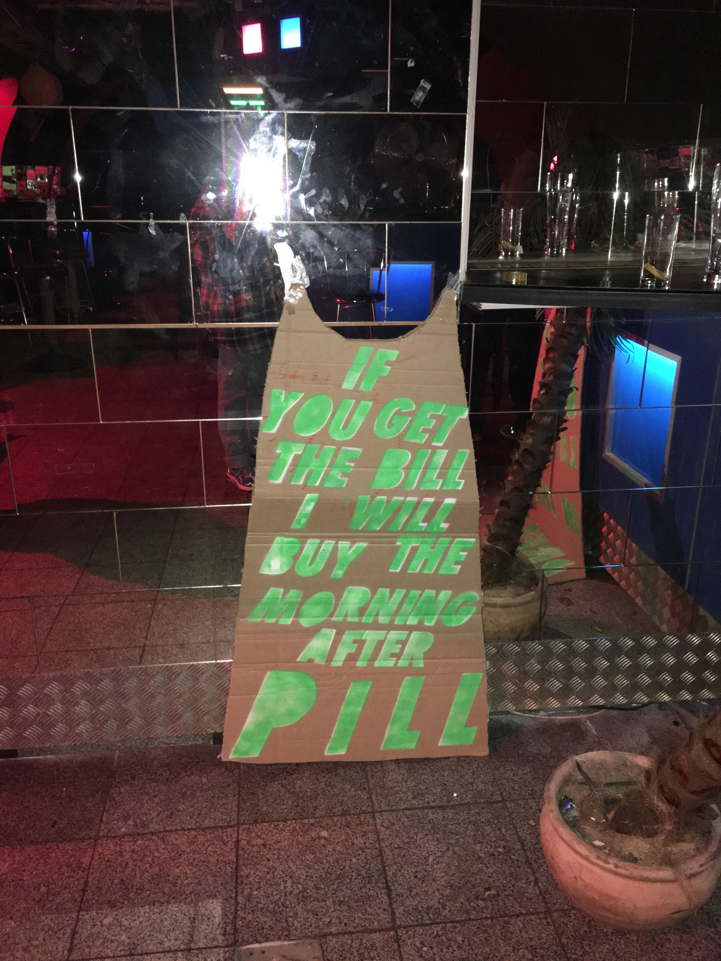 A cardboard dress with bright green lettering displayed against a mirrored wall.