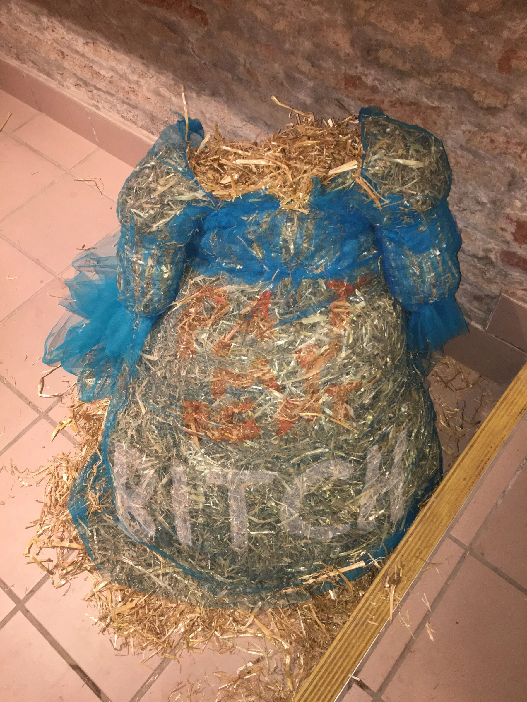 A blue tulle costume filled with straw on a tiled floor.