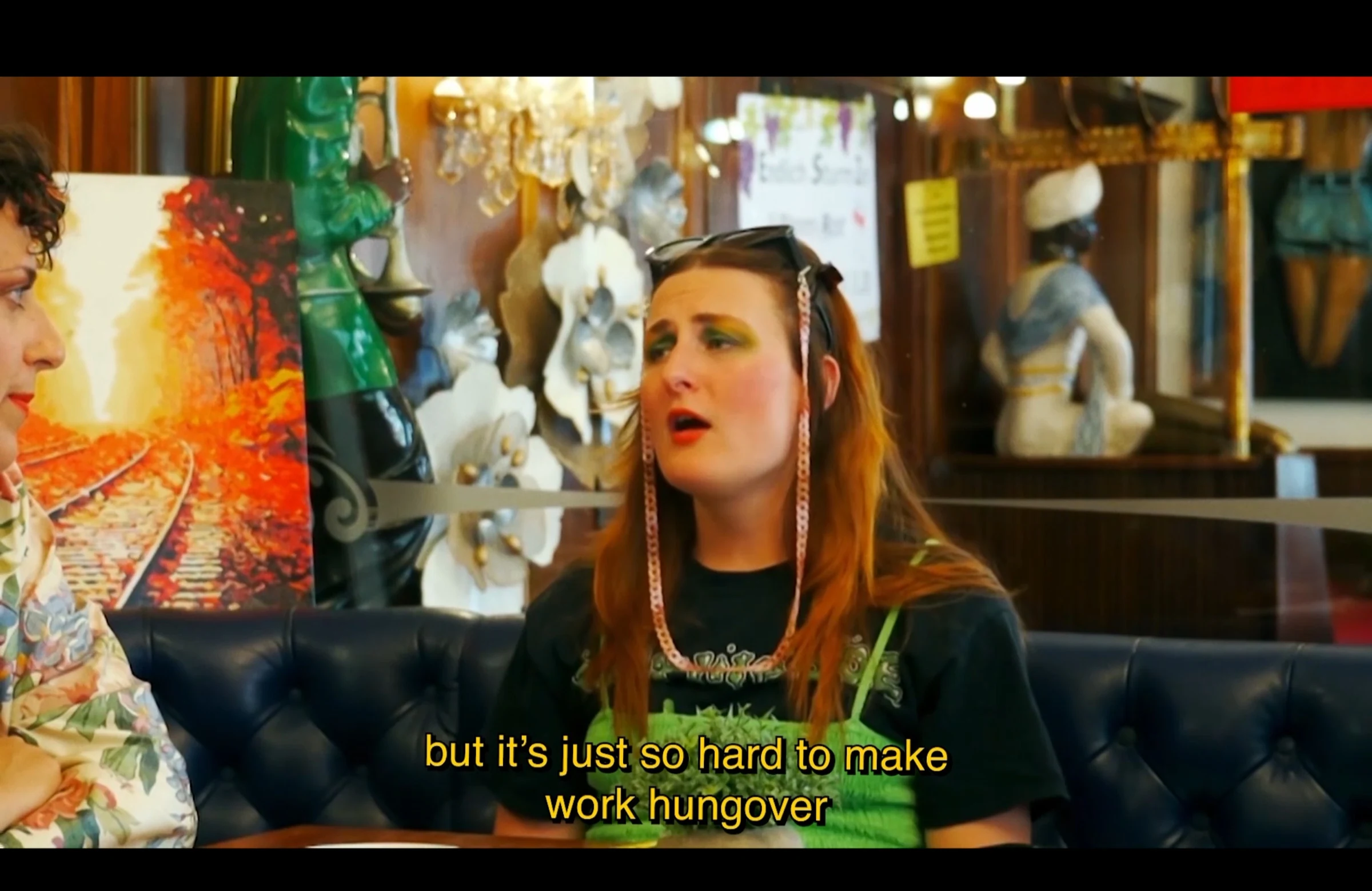 A red-haired character in a café discussing the difficulty of working while hungover.