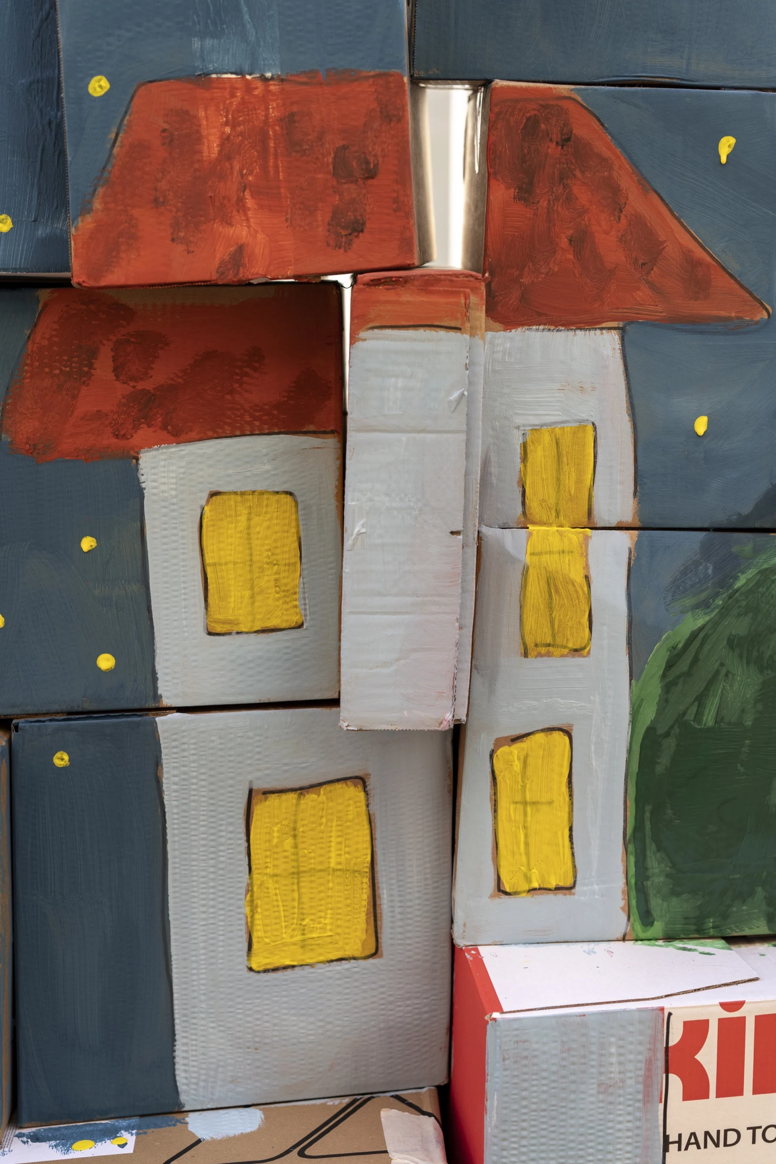 Detail of a cardboard castle with red roofs and yellow windows.