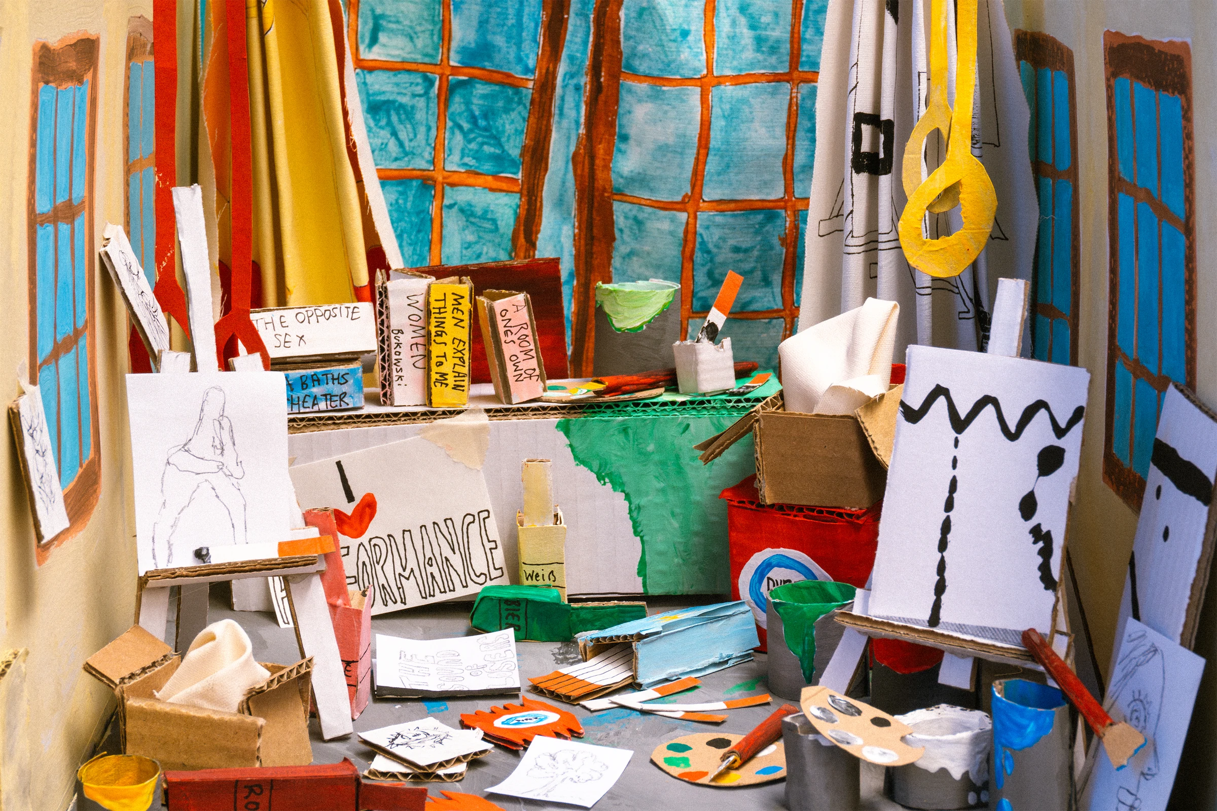 A handmade cardboard art studio with blue windows, easels, books and colourful art supplies.