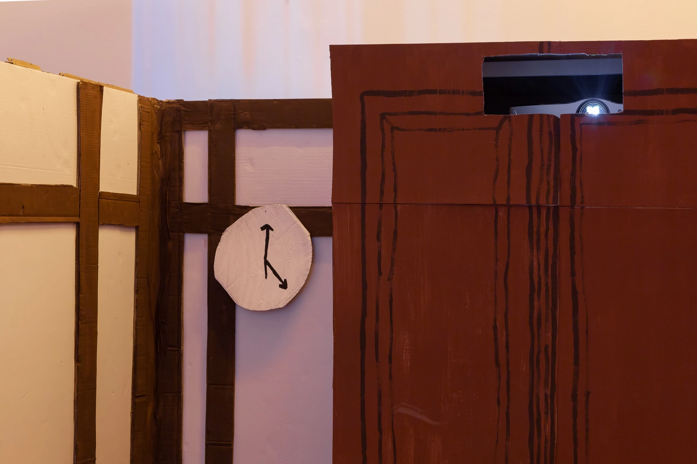 A cardboard door with a projector above it and a handmade wall clock.