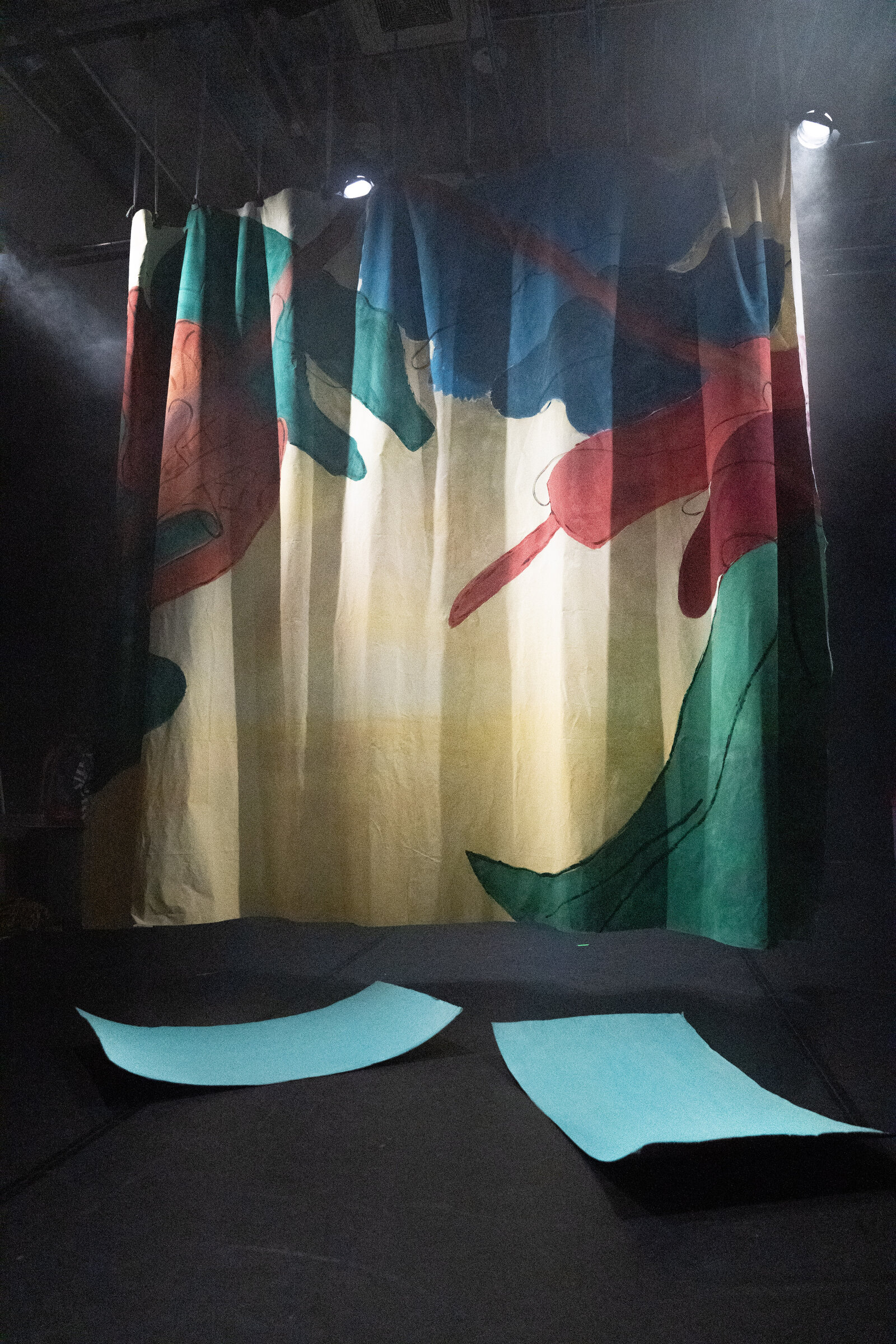The colourful leaf backdrop hanging on stage beneath spotlights, with painted shapes on the floor.