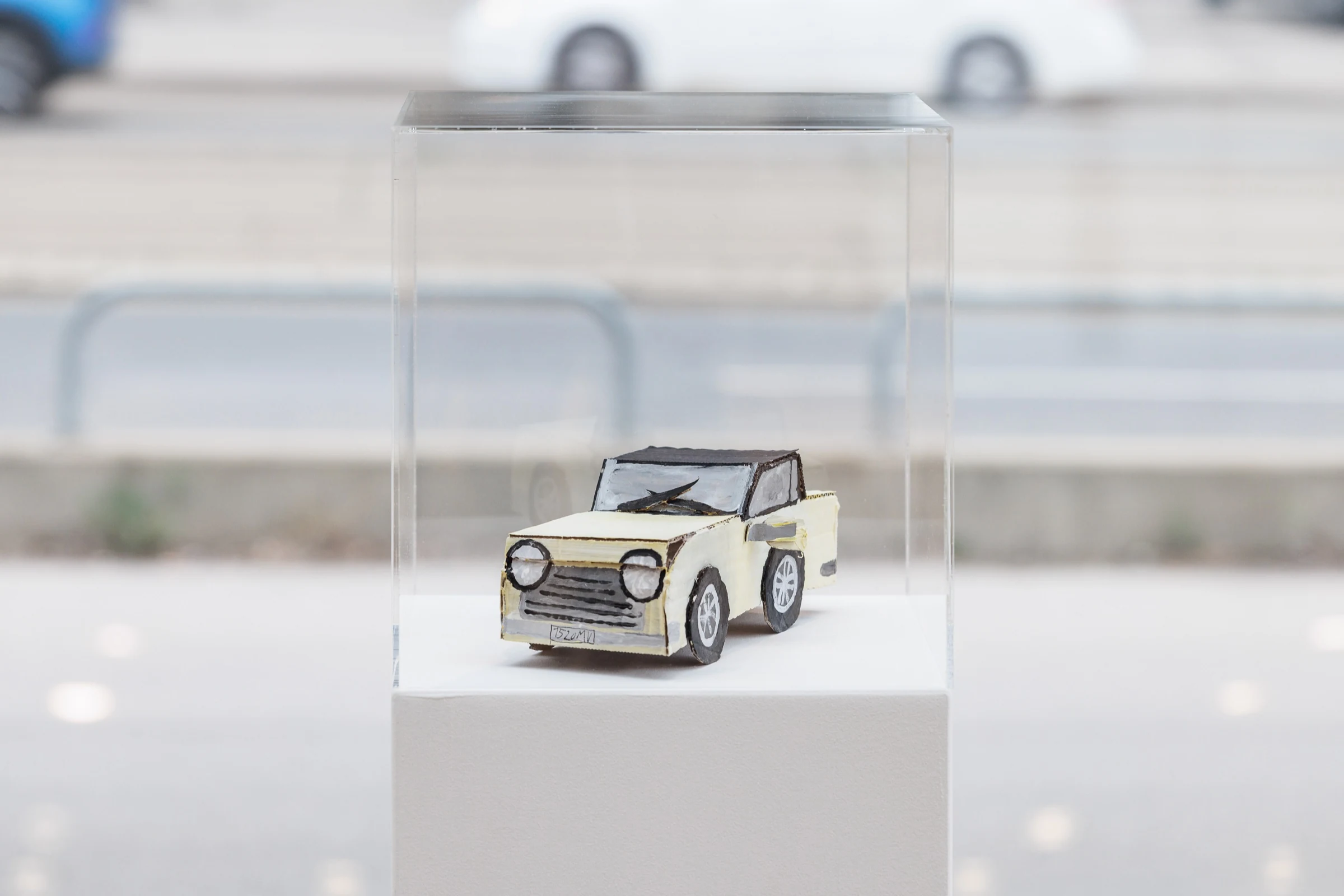 A small cream-coloured cardboard car inside a transparent display case.