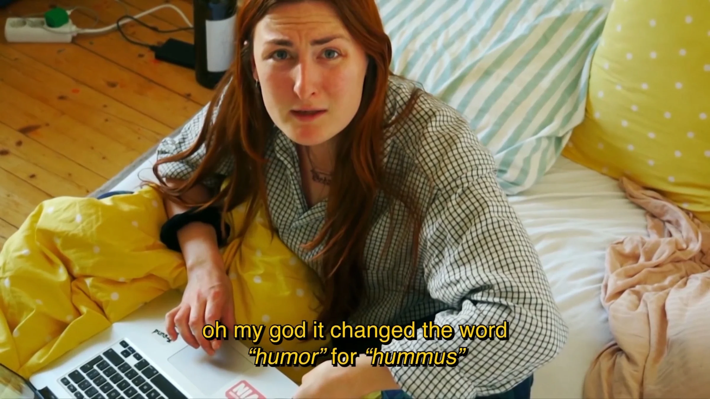 A character looking up from a laptop on a bed, with a subtitle about humor and hummus.