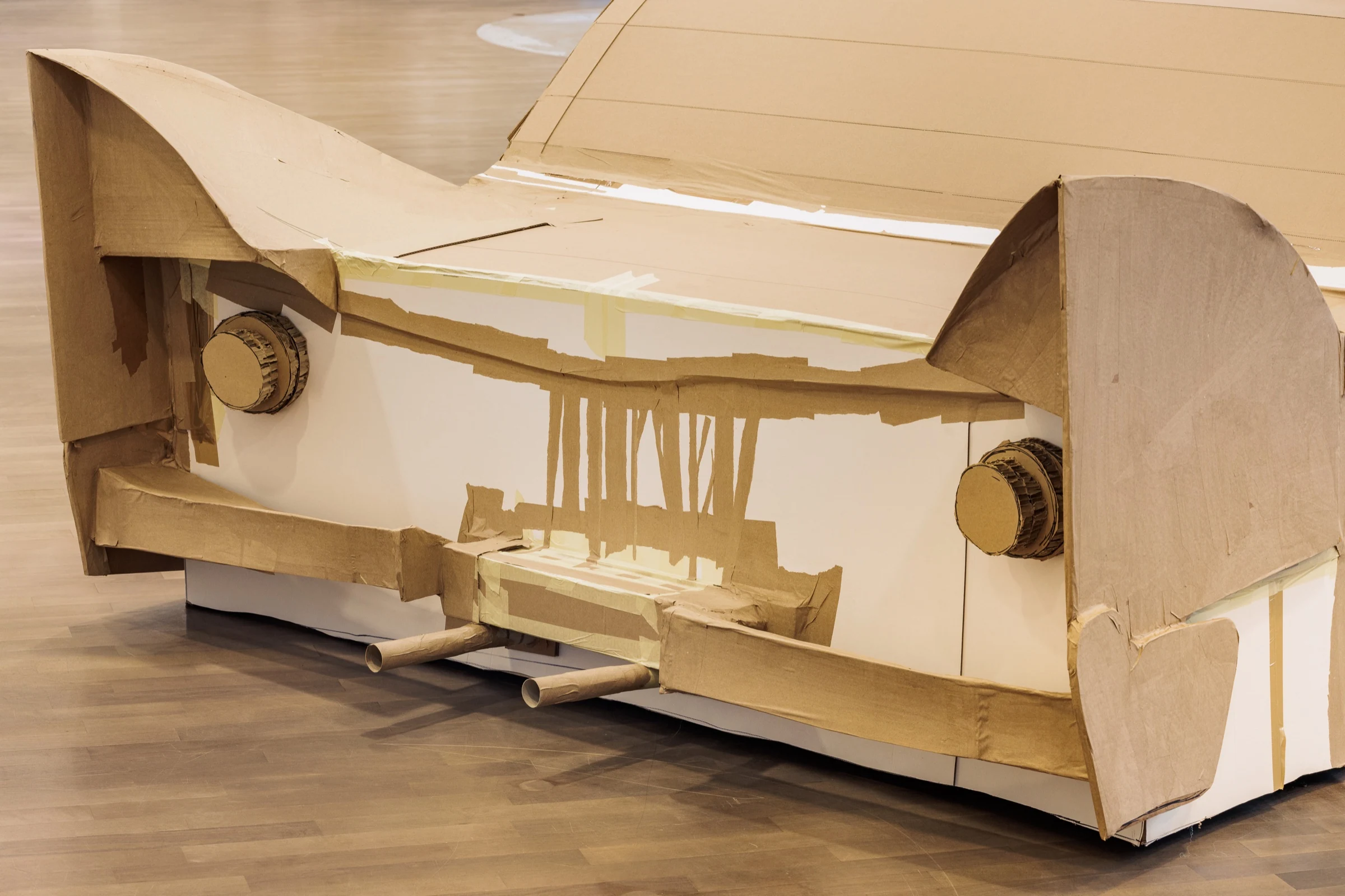 A close-up of the rear of a full-size cardboard car with handmade exhaust pipes.