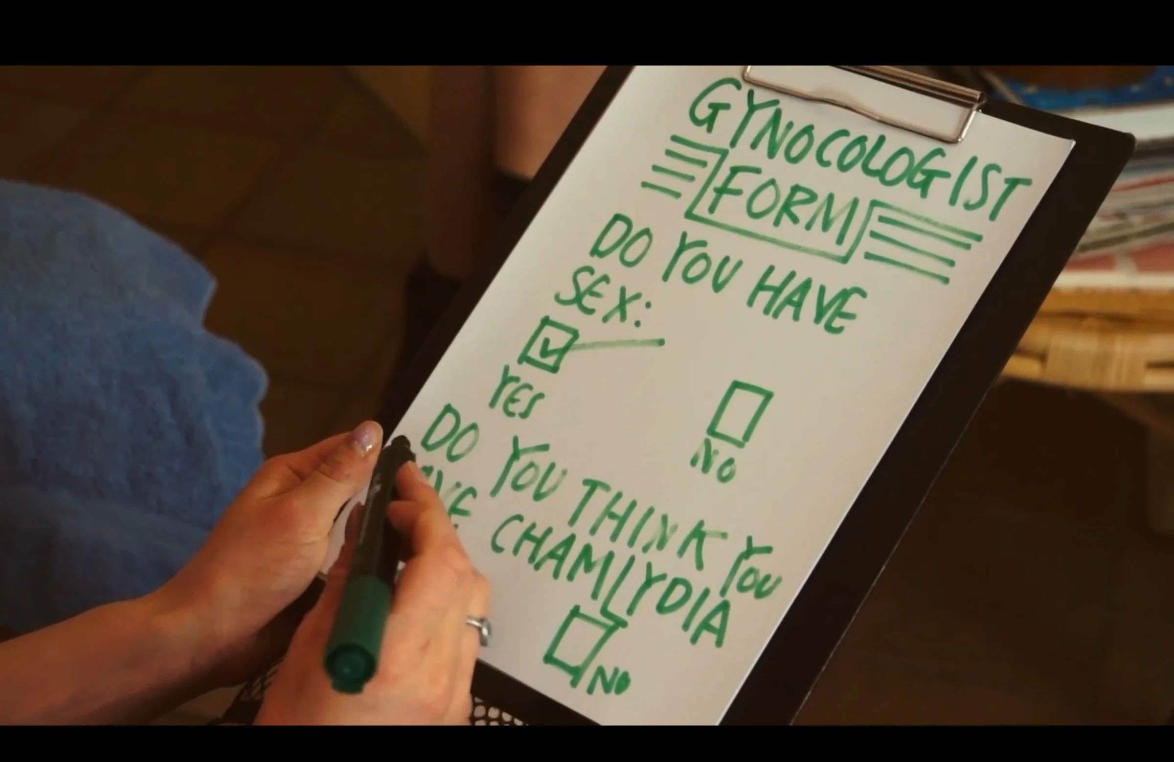 A close-up of a hand completing a hand-lettered gynecologist form on a clipboard.