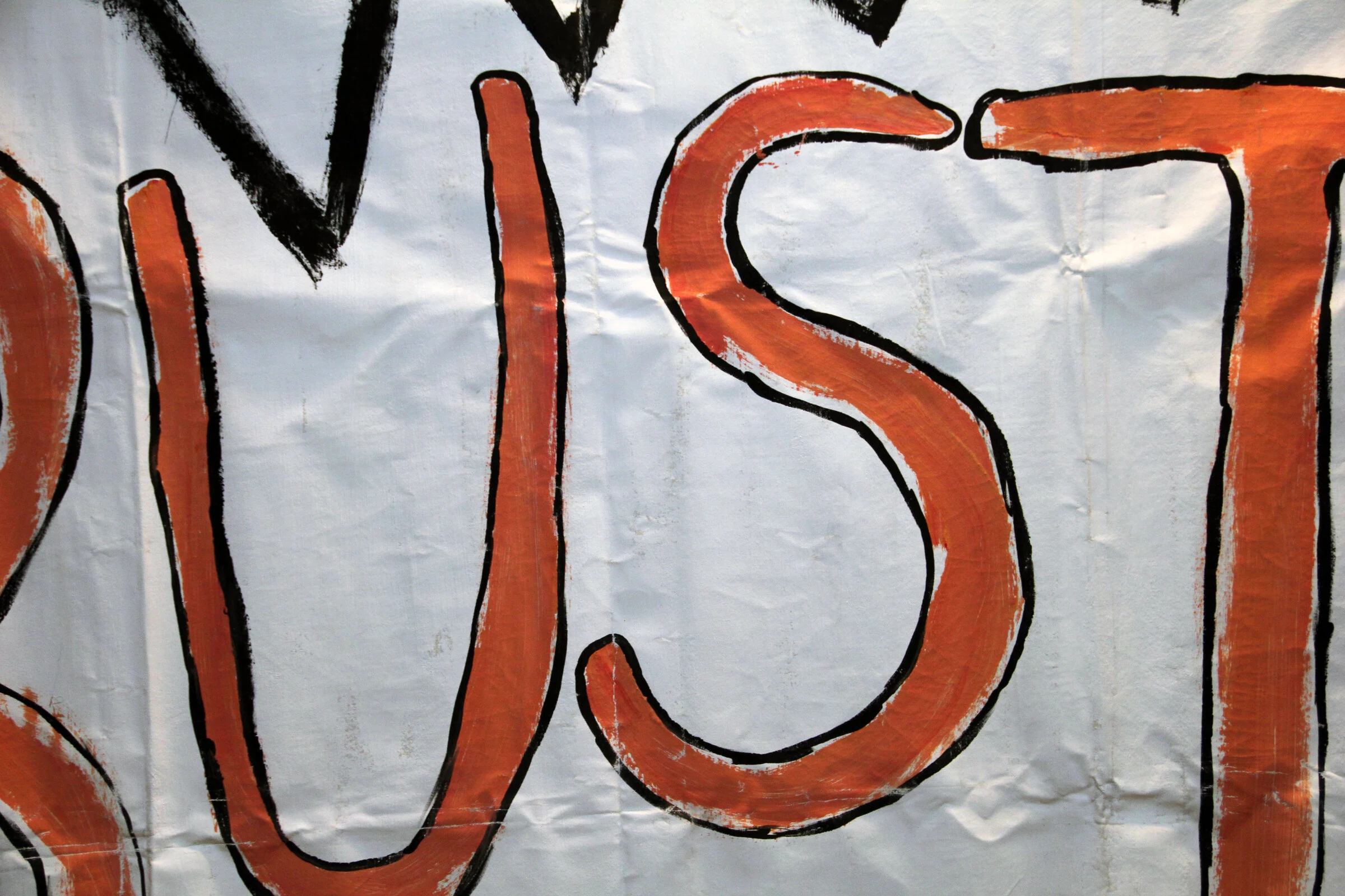 A close-up of orange BUST lettering outlined in black on white canvas.