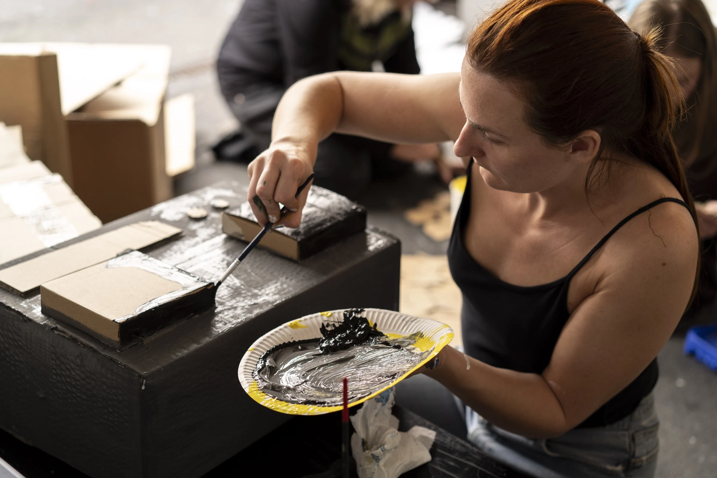 Charlotte Gash painting a cardboard box prop with a paper plate palette.