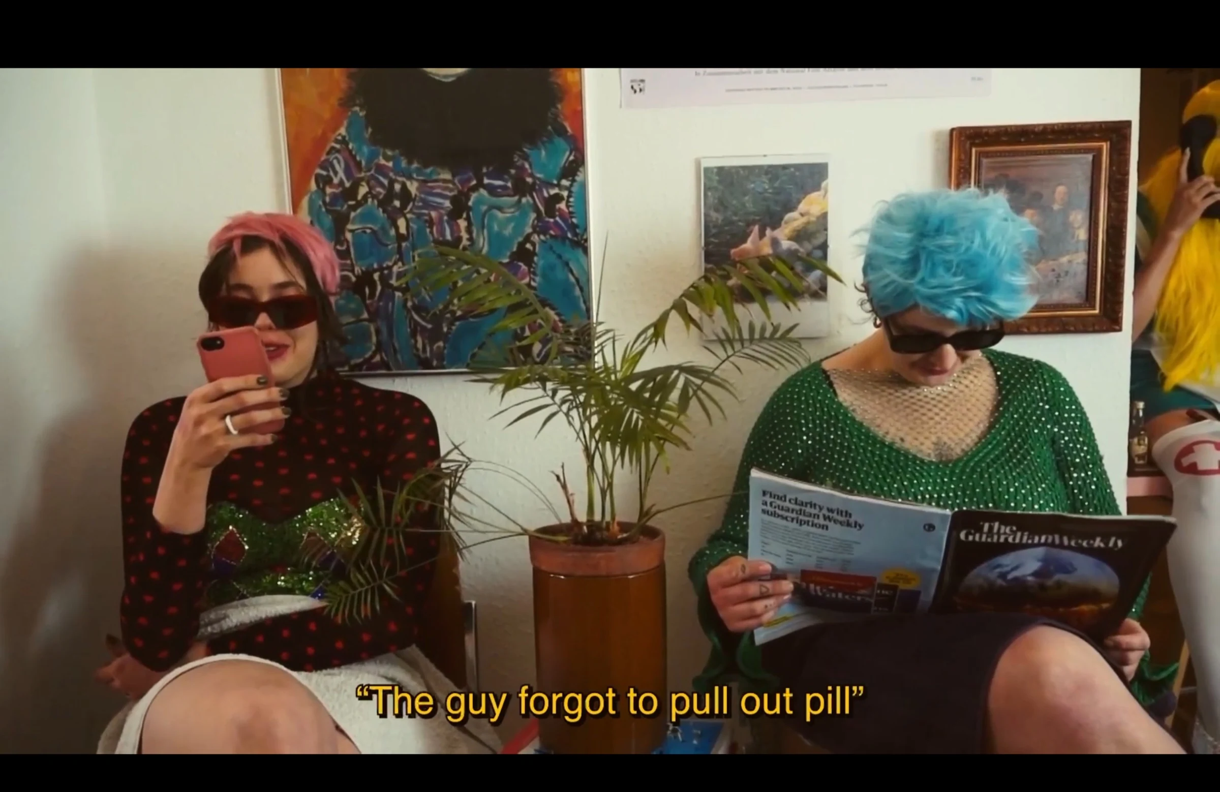 Two characters wearing colourful wigs and sunglasses in a waiting room, one using a phone and one reading a magazine.