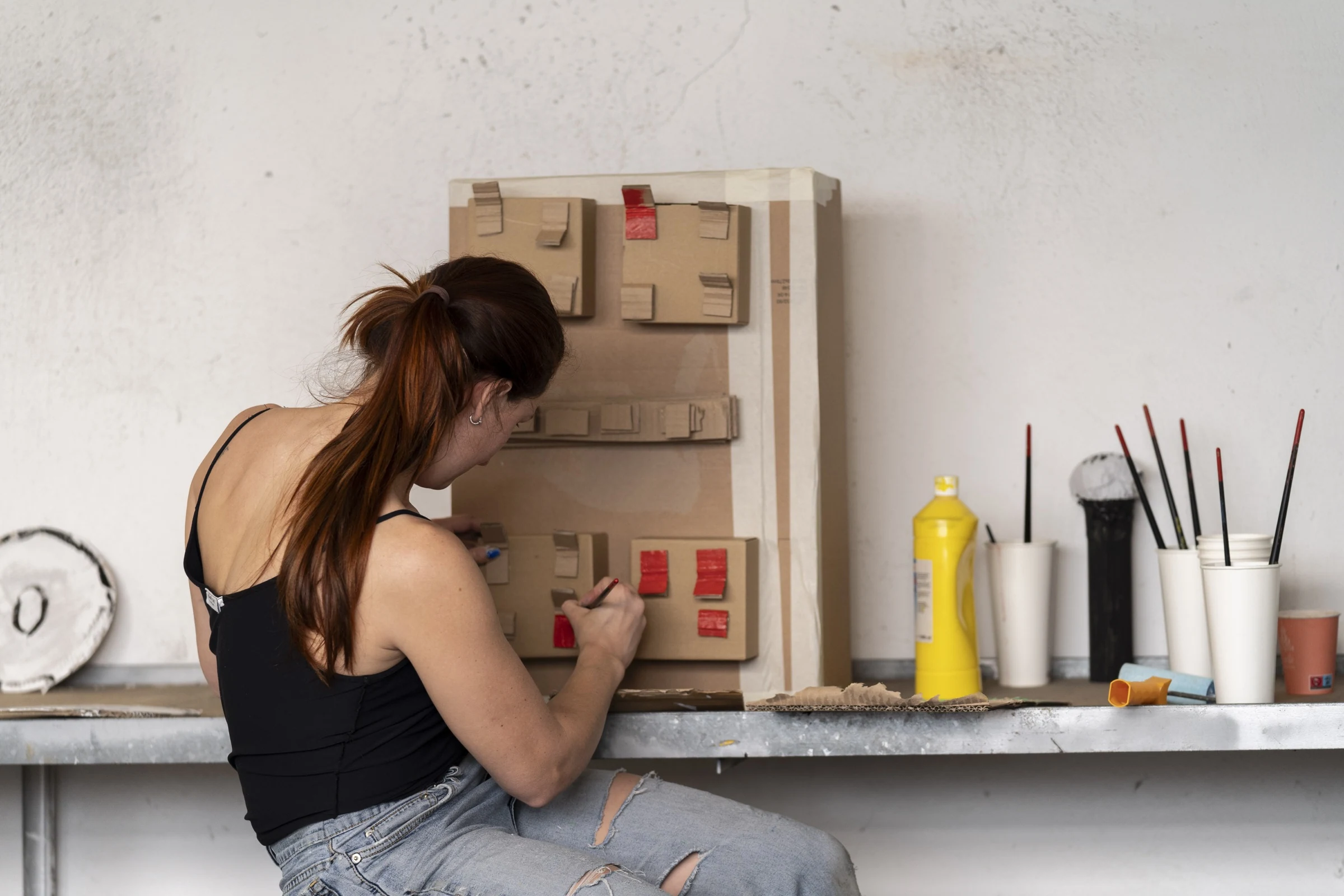 Charlotte Gash painting red switches on a cardboard electrical panel.
