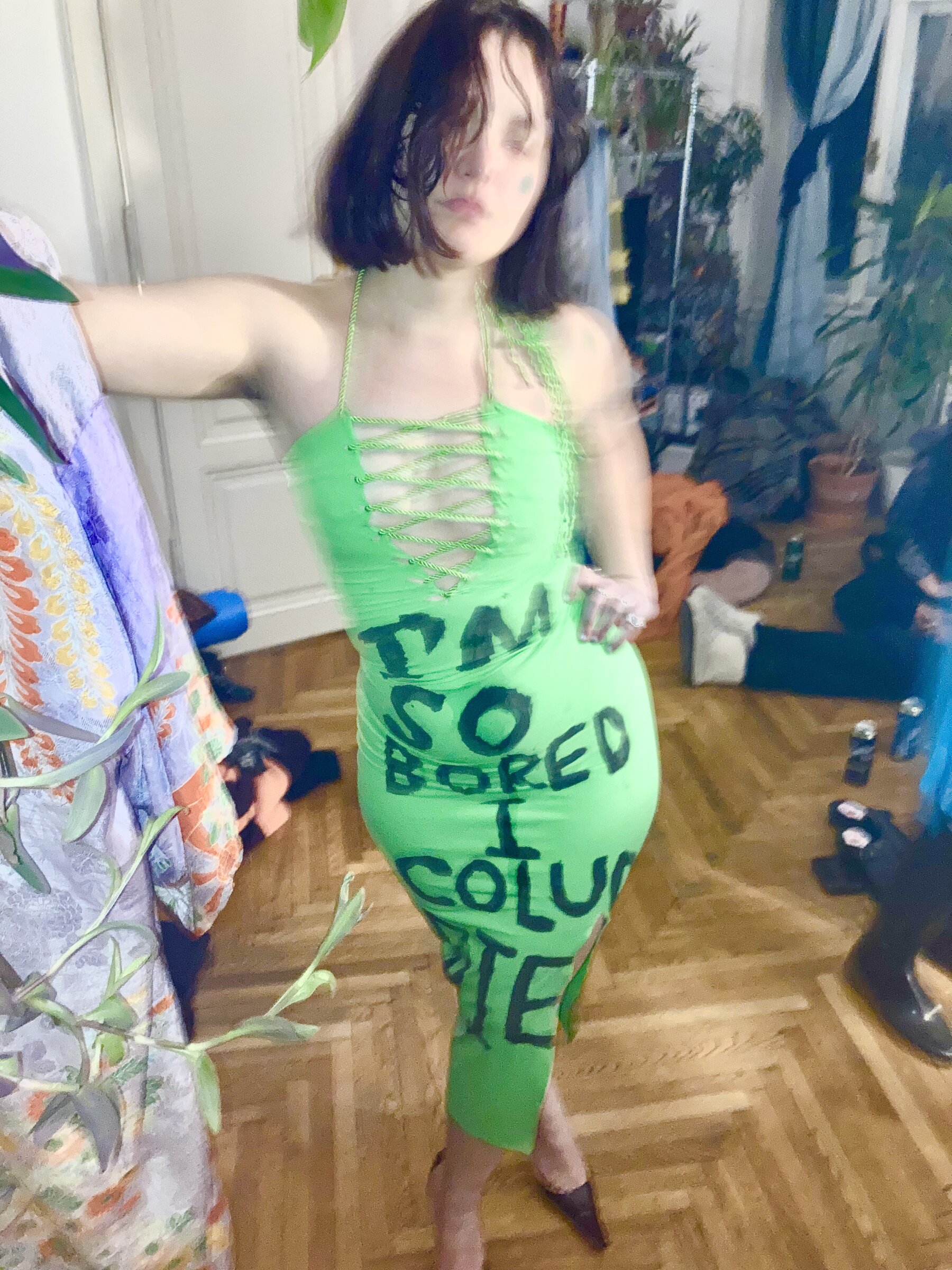 A performer modelling a green dress with black lettering in an art studio.