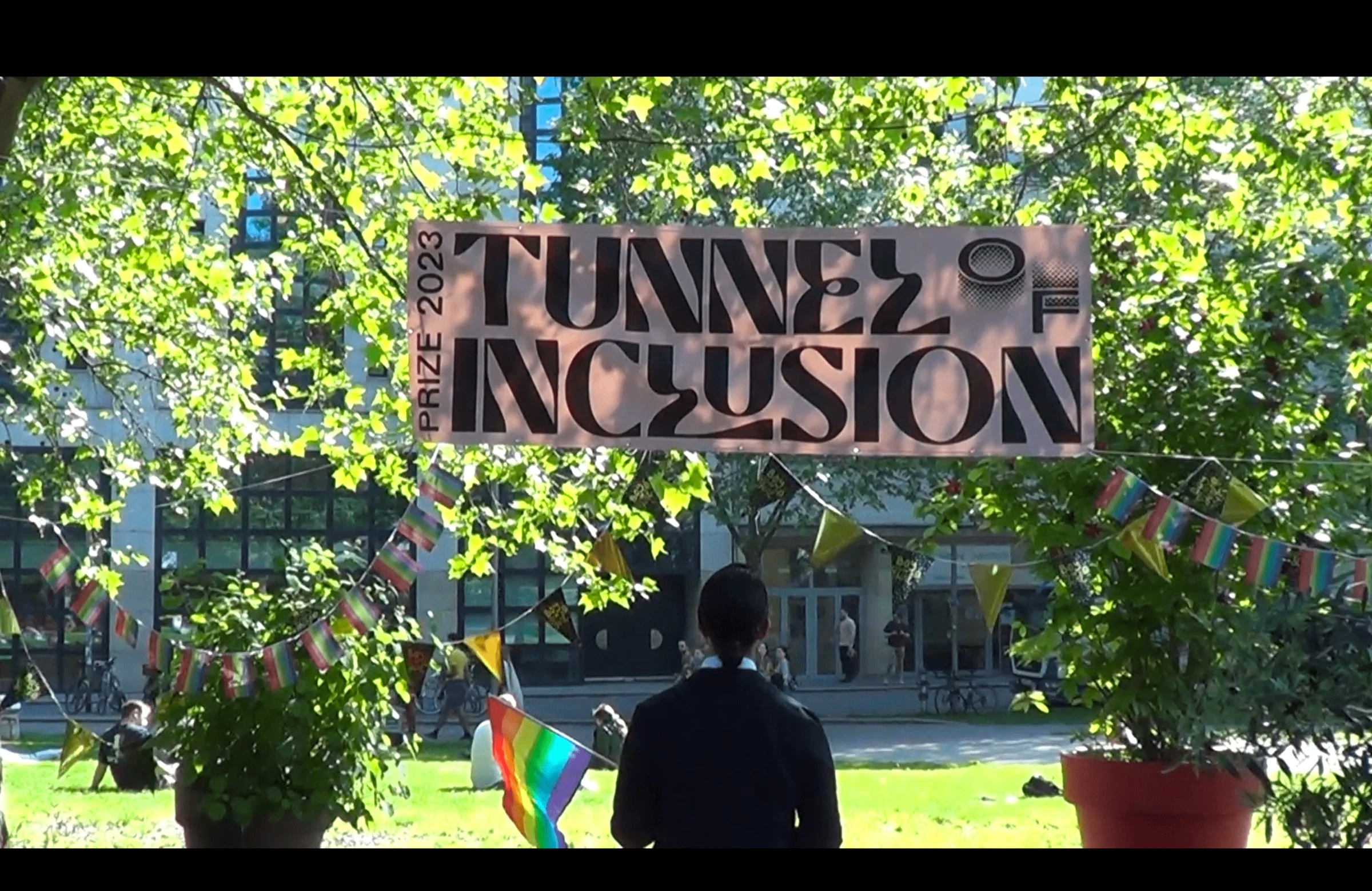 A Tunnel of Inclusion Prize 2023 banner hanging among trees and colourful flags.