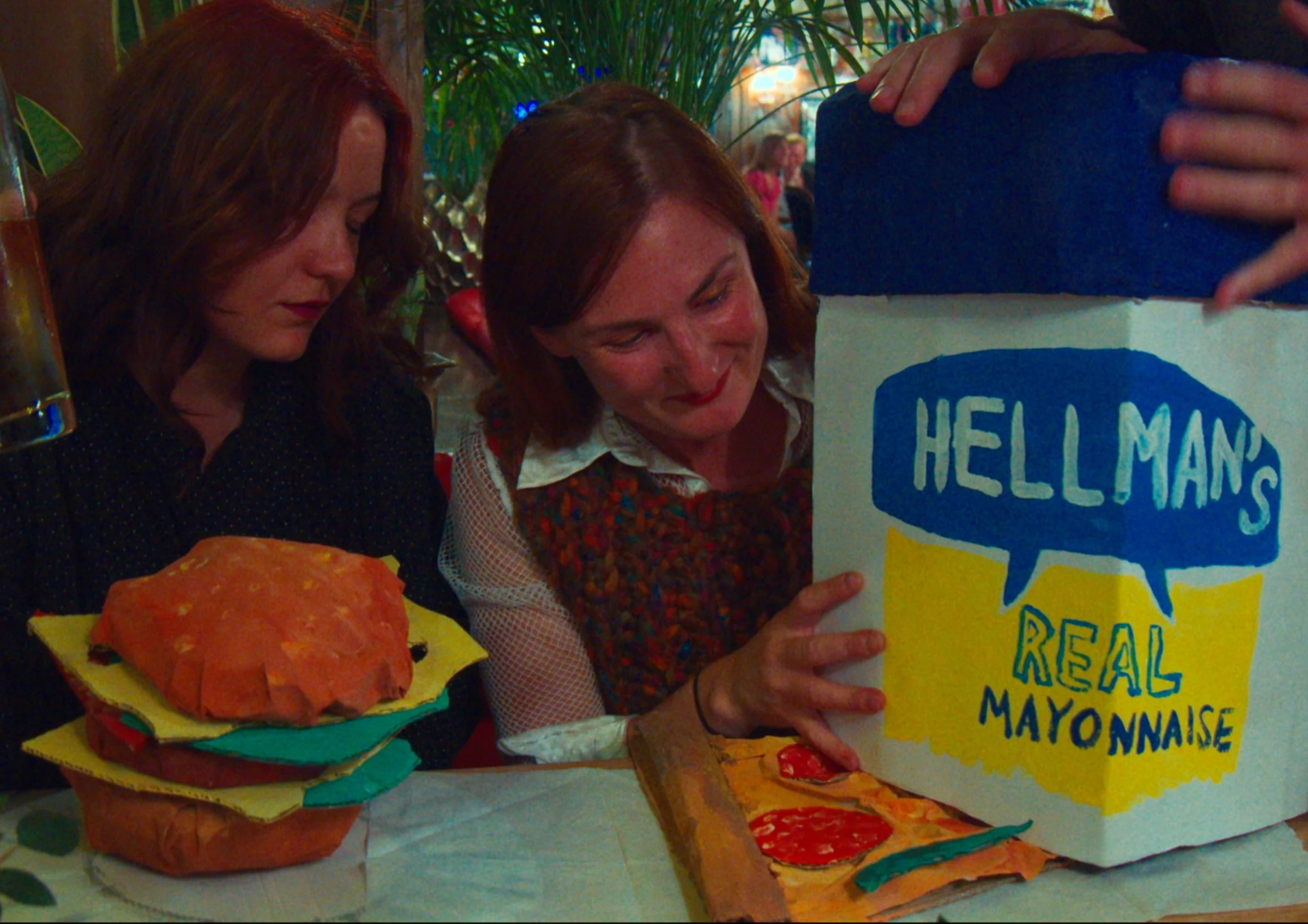 Two characters beside a giant handmade mayonnaise jar and hamburger.