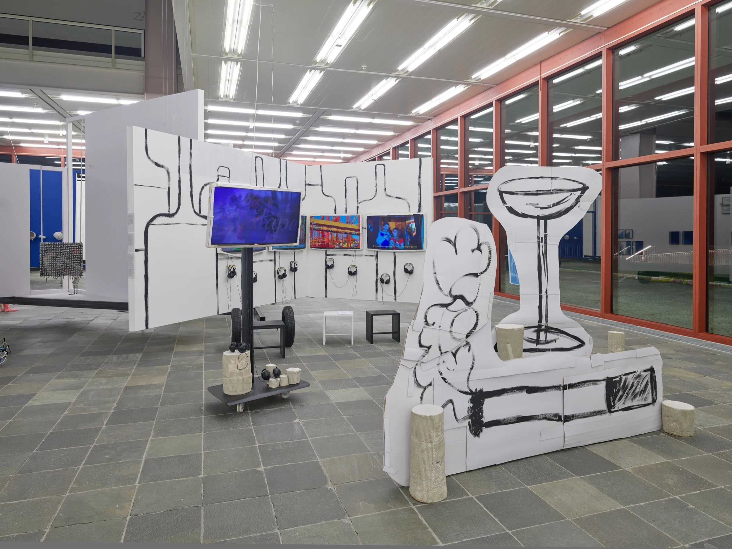 LOCATION installed with video screens, headphones and oversized cardboard sculptures in the exhibition hall.