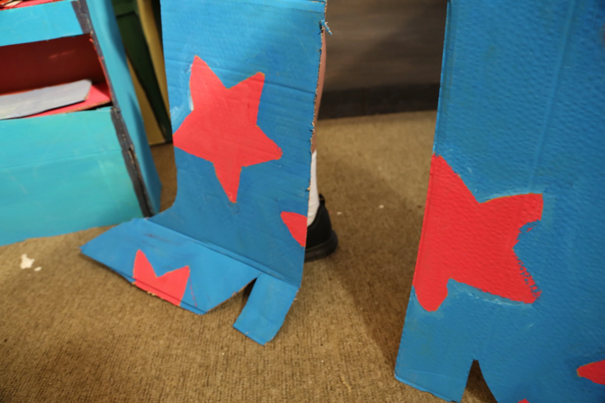 A close-up of blue cardboard boots painted with red stars.