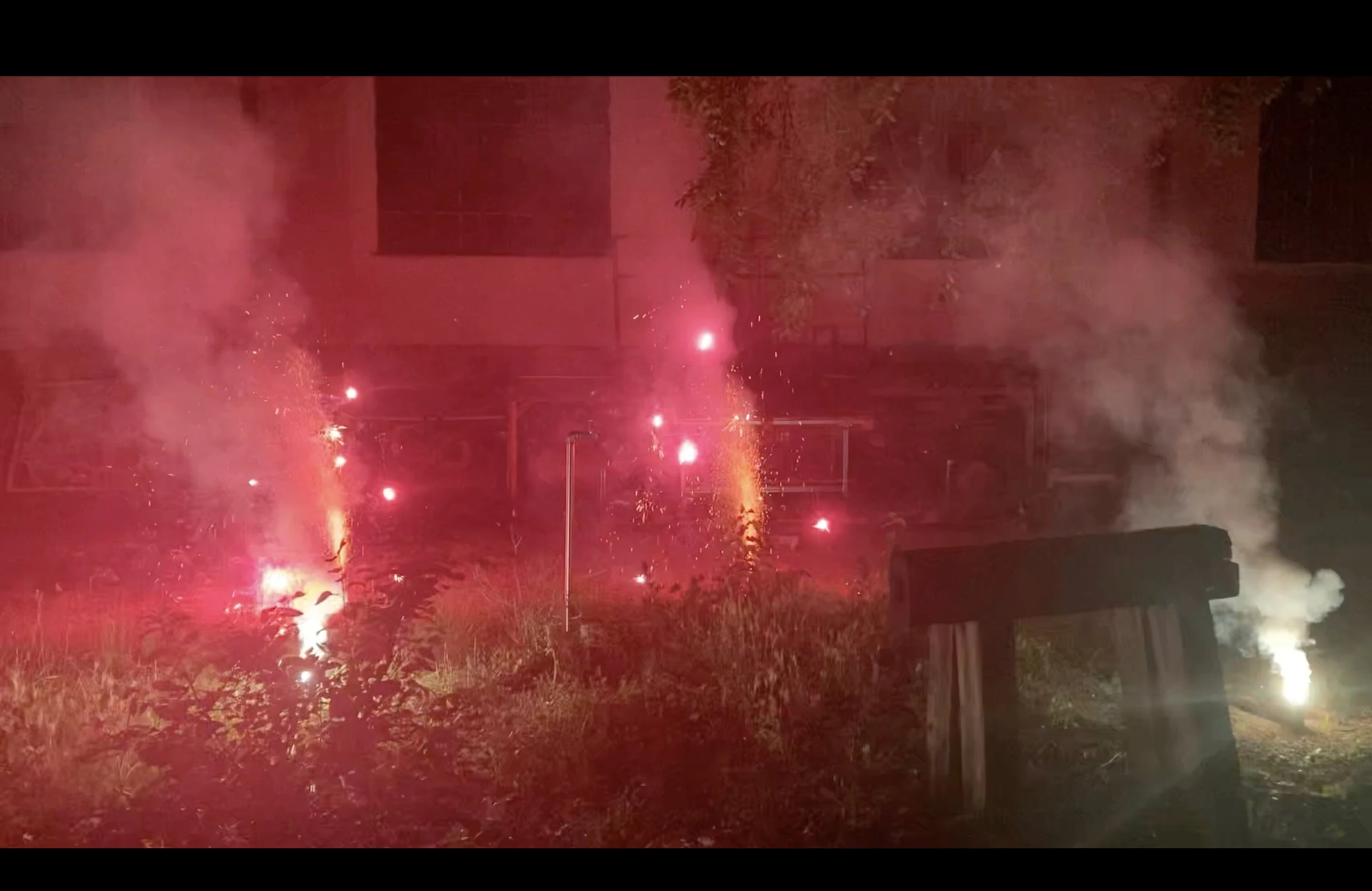Red fireworks flaring beside a wooden bench amid thick smoke.