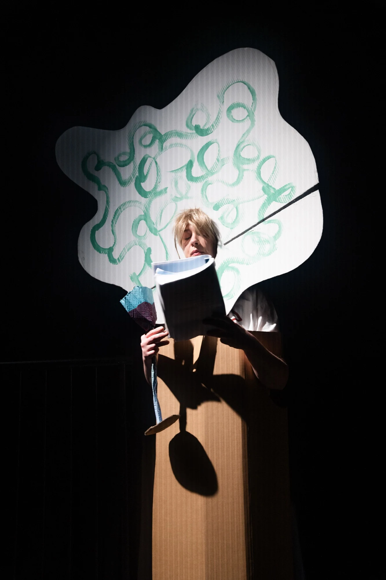 A performer wearing a cardboard tree costume and reading a script.