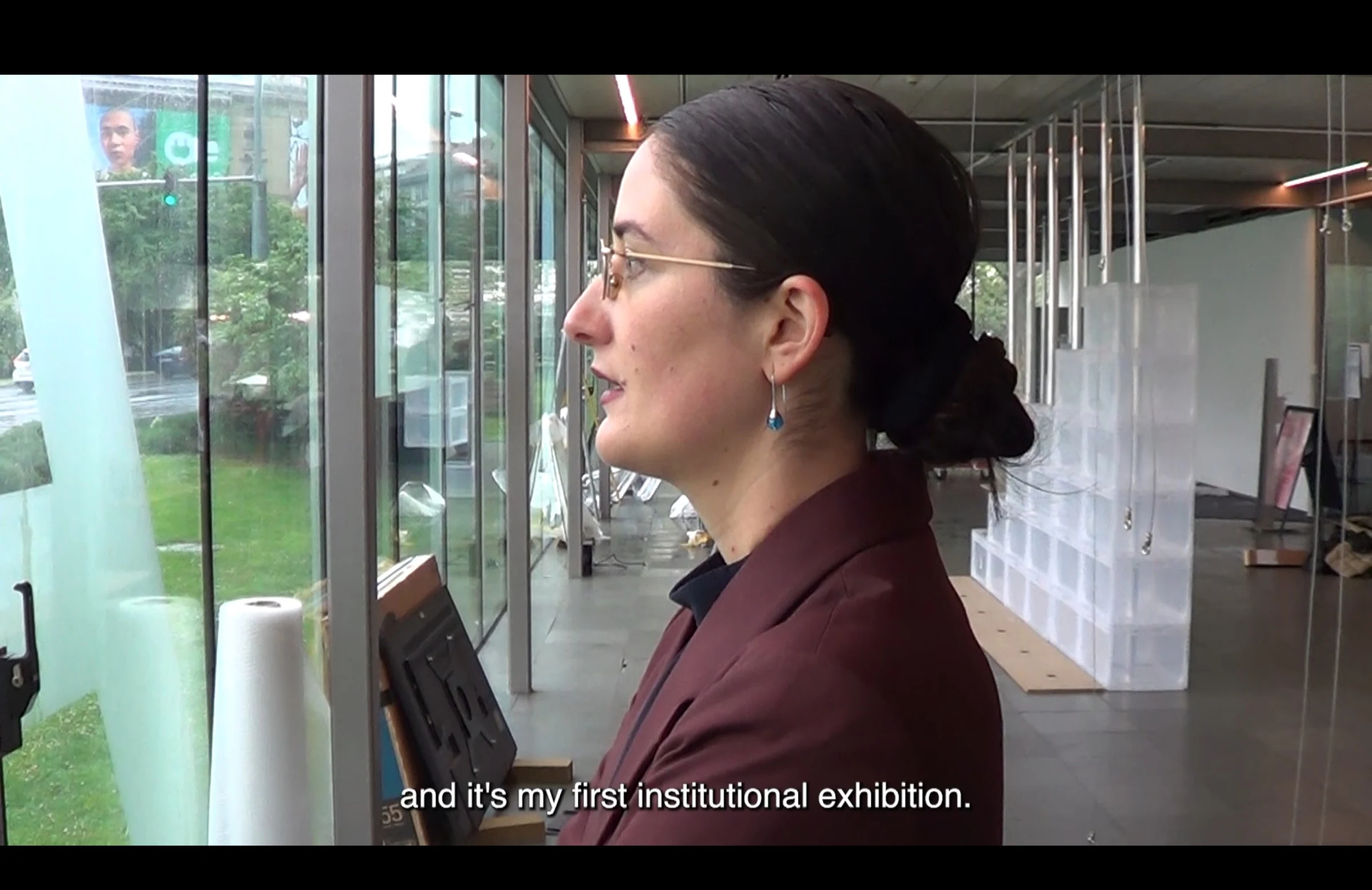 A film still of a curator speaking inside the gallery about her first institutional exhibition.