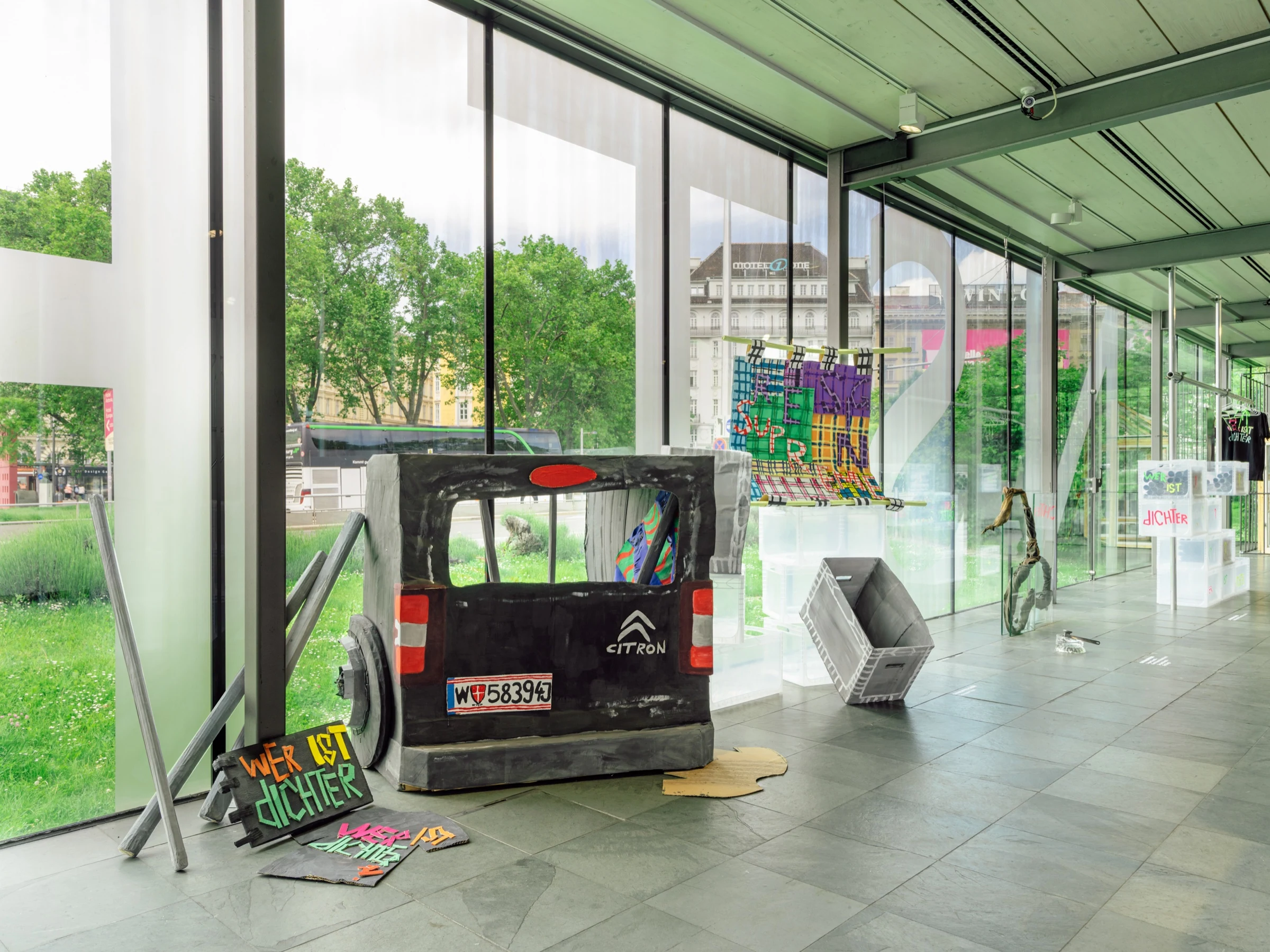 A wide view of the cardboard van, textiles and crates along the gallery windows.