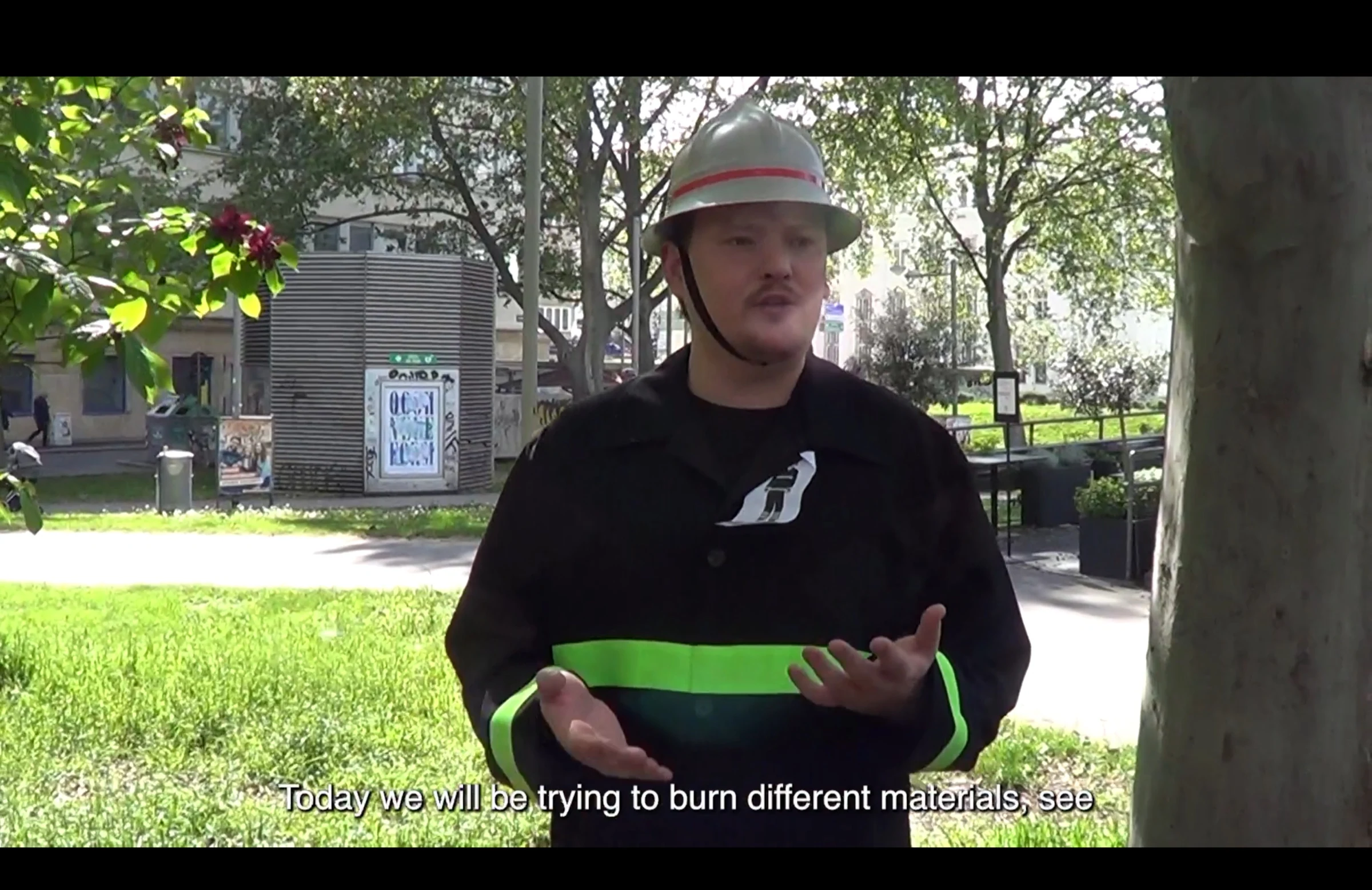 A performer in a firefighter costume explaining a materials demonstration outdoors.