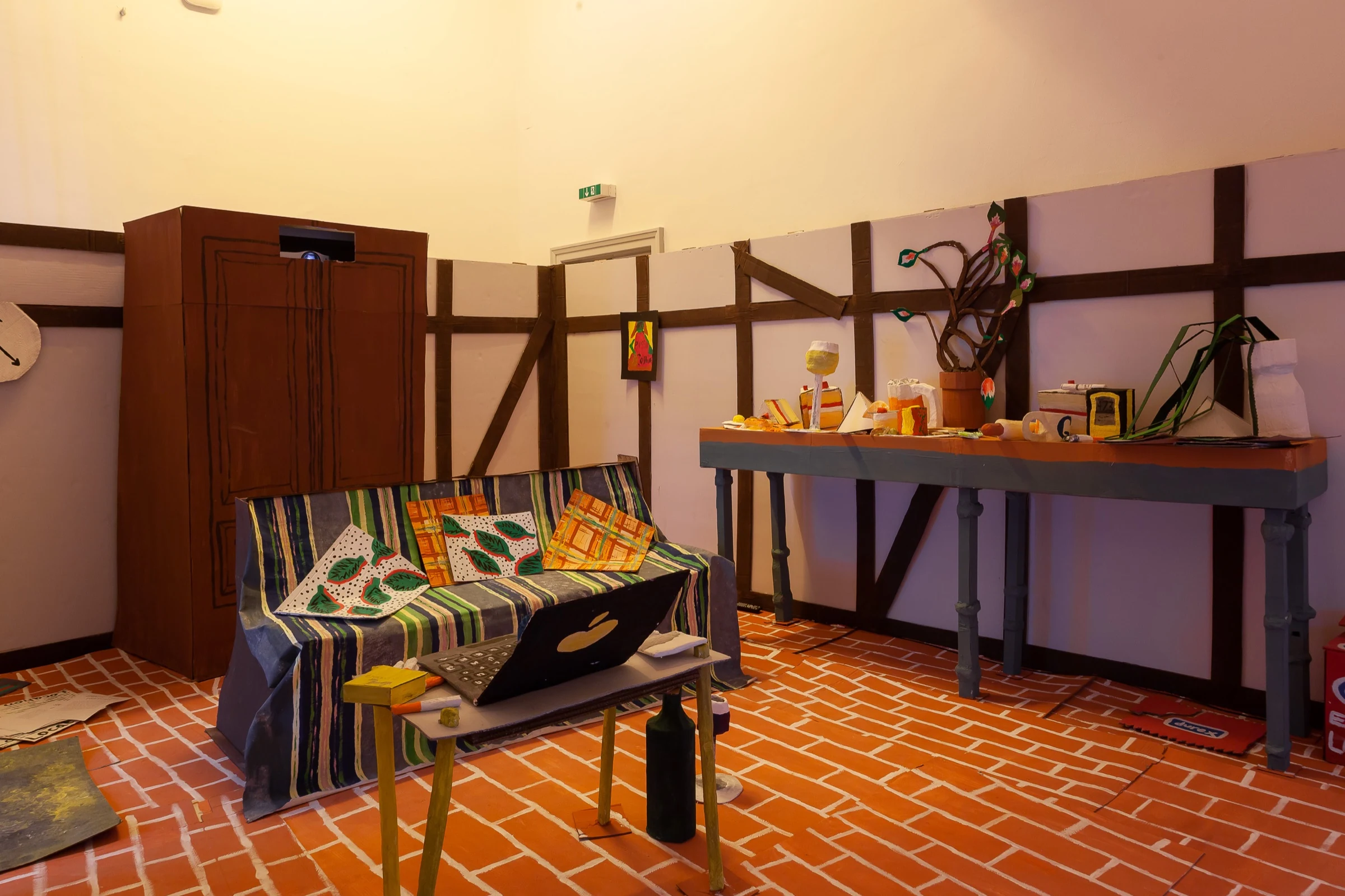 A wide view of the installation with a wardrobe, sofa, table and kitchen counter.