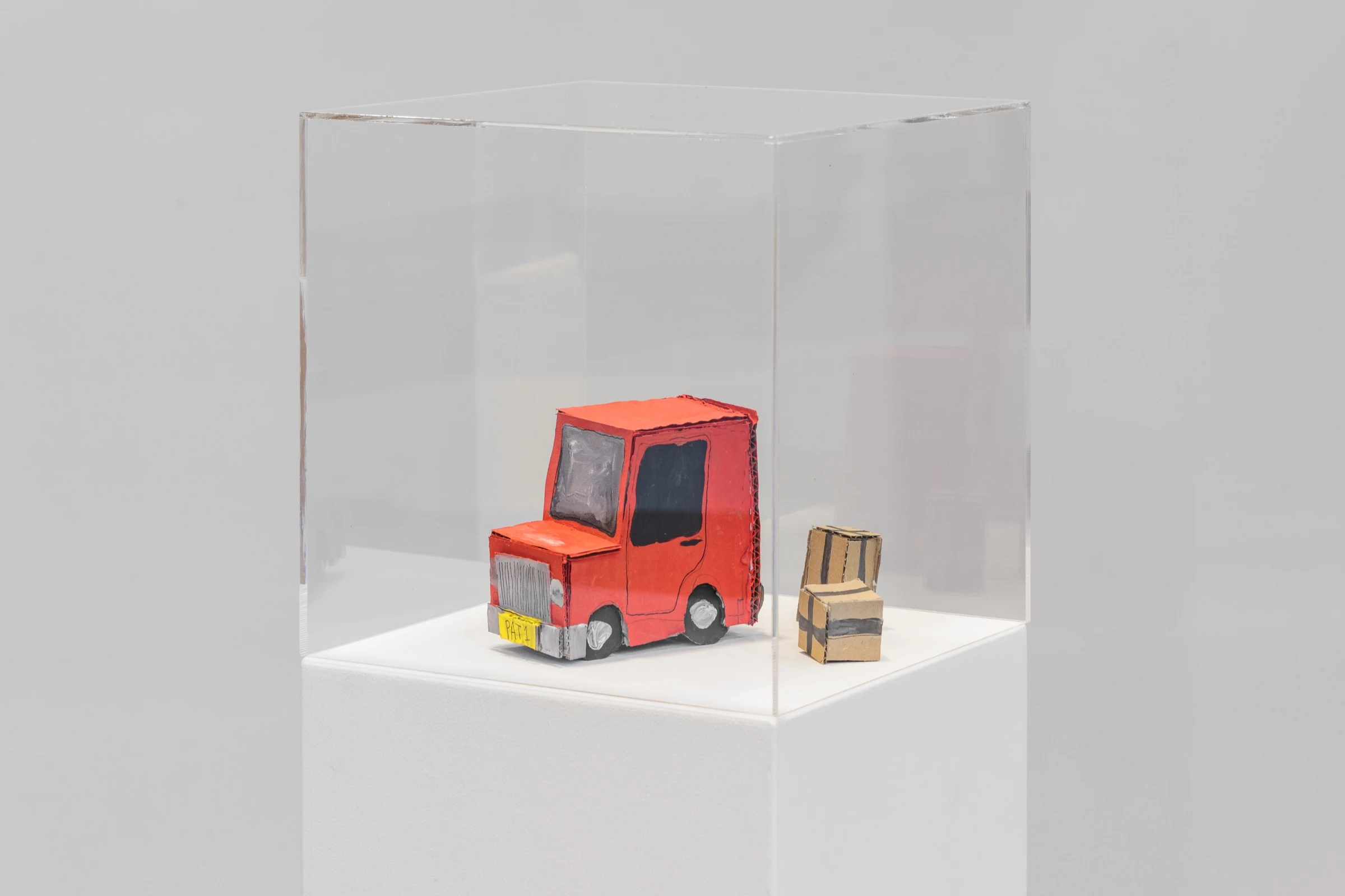 A red cardboard delivery van and a small parcel inside a transparent display case.