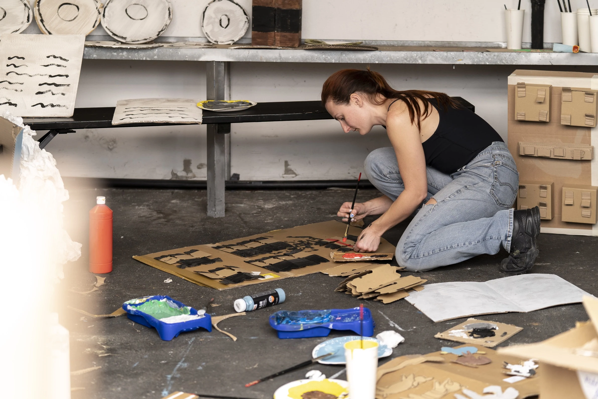 Charlotte Gash kneeling on the floor to paint cardboard animal cutouts.