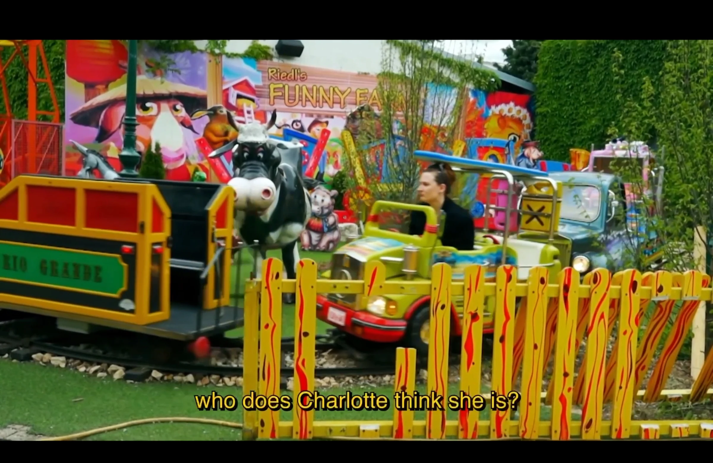 A character riding a colourful amusement park train, subtitled Who does Charlotte think she is?