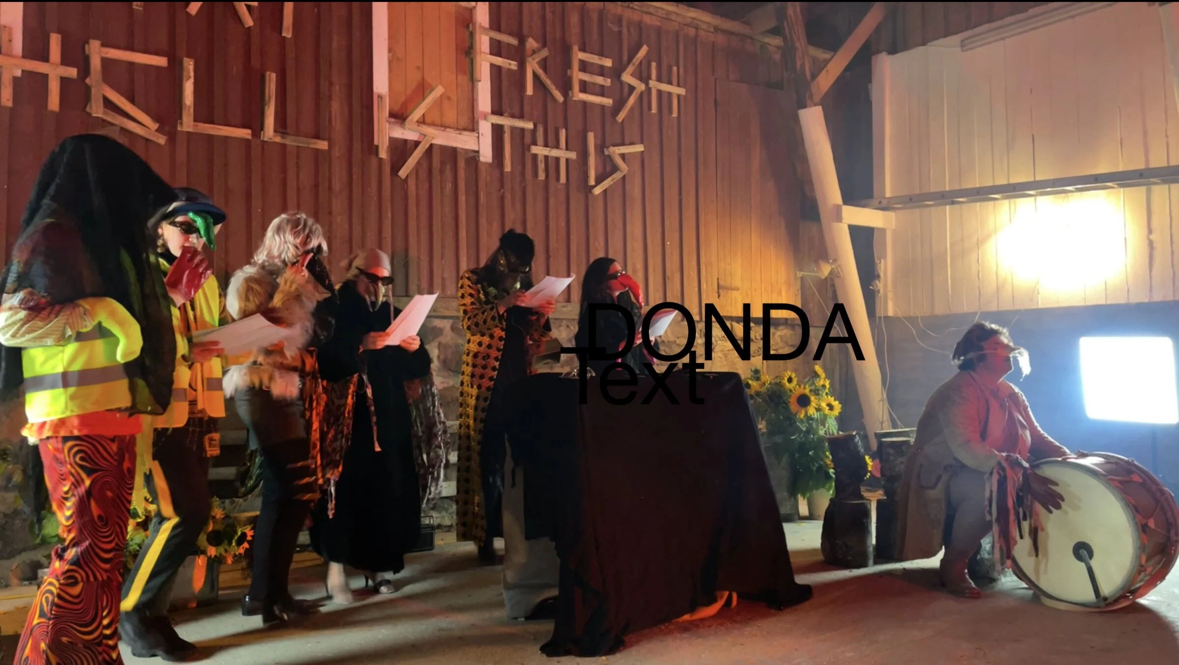 Masked performers reading scripts beside a large drum in a barn, with DONDA text overlaid.