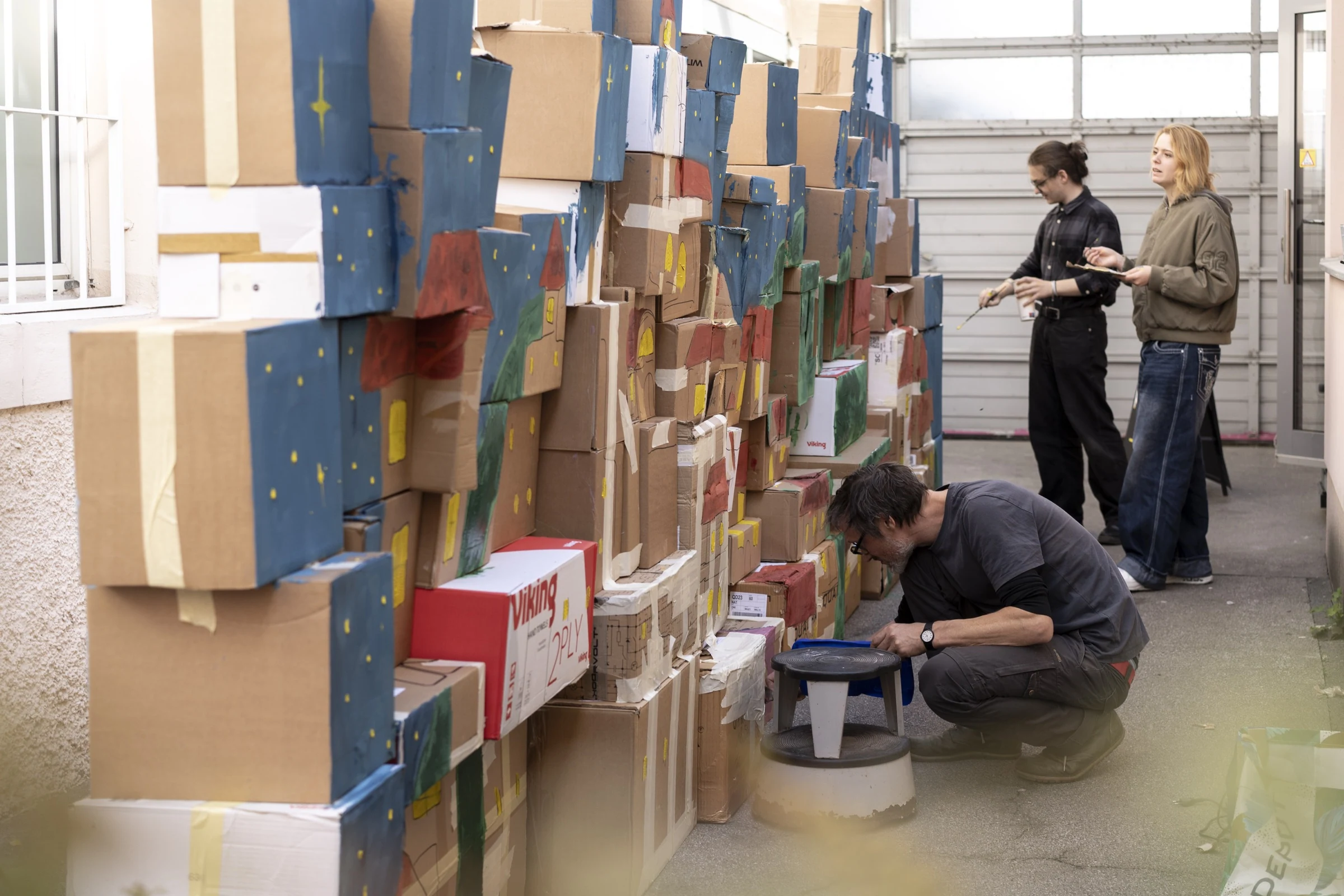 Participants painting a castle scene on a wall of stacked cardboard boxes.