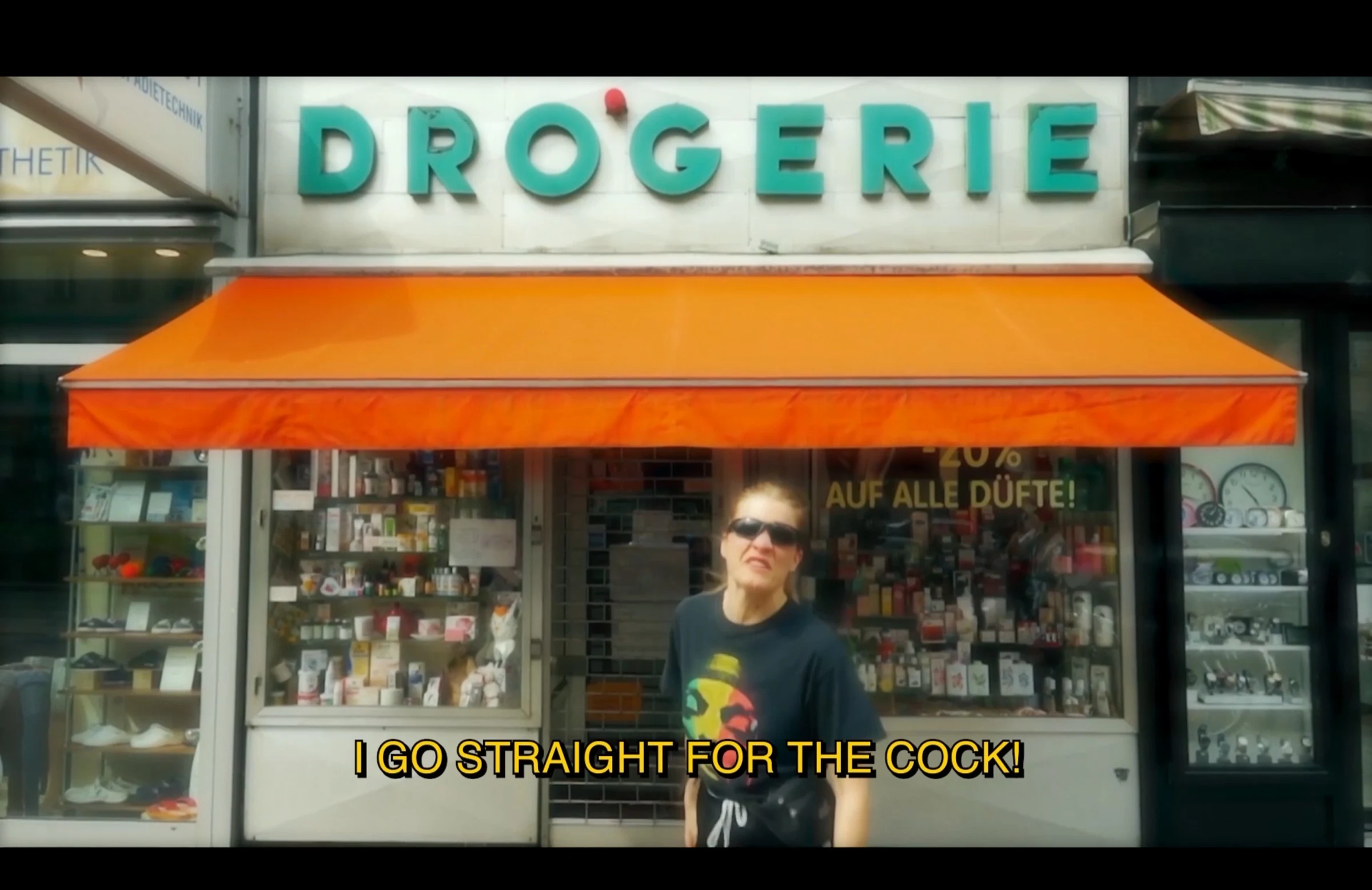 A character wearing sunglasses outside a drugstore with an orange awning.