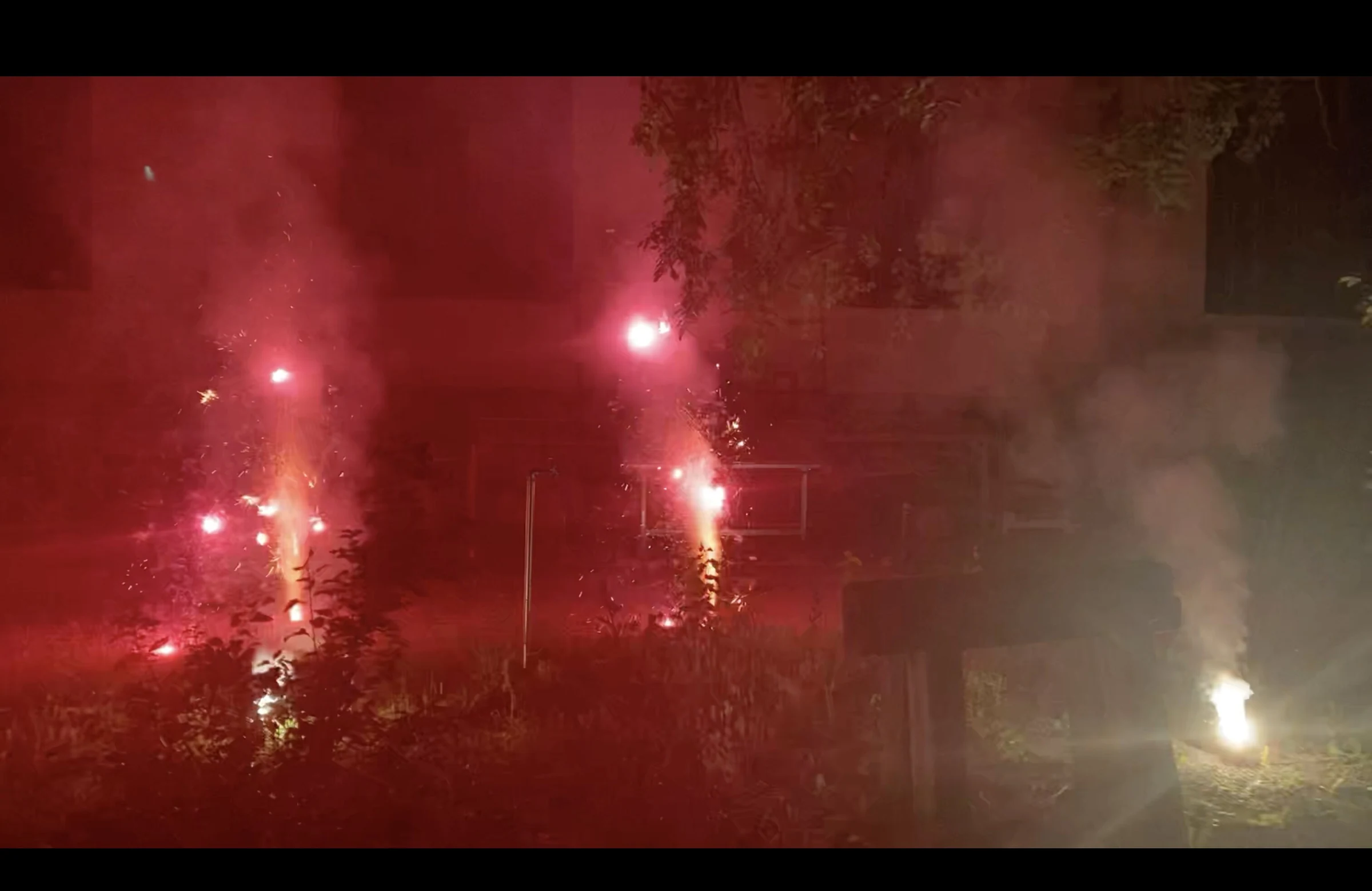 Red fireworks and smoke lighting the courtyard in front of a building.