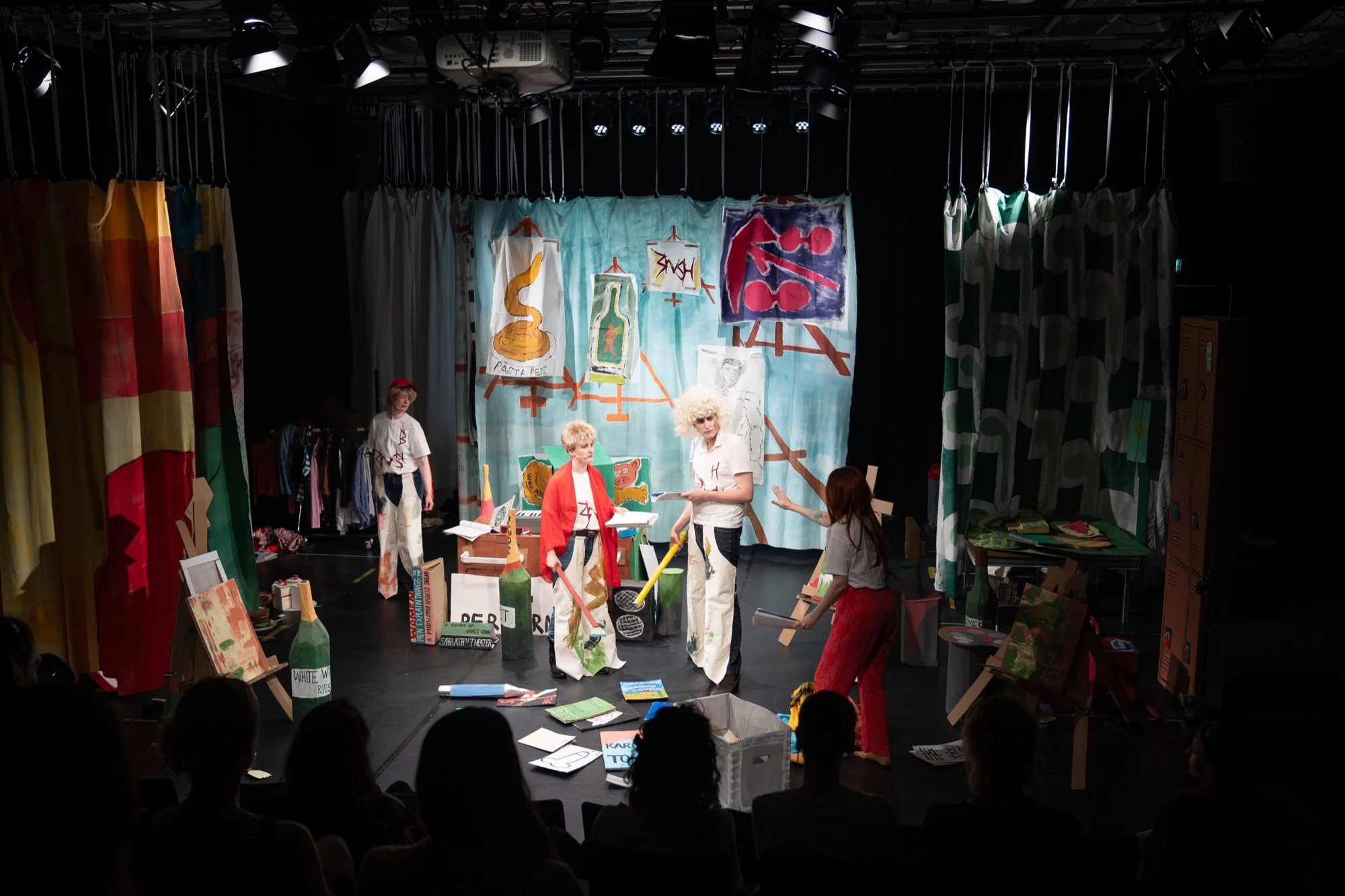 Performers on a stage filled with handmade art props, with the audience in the foreground.