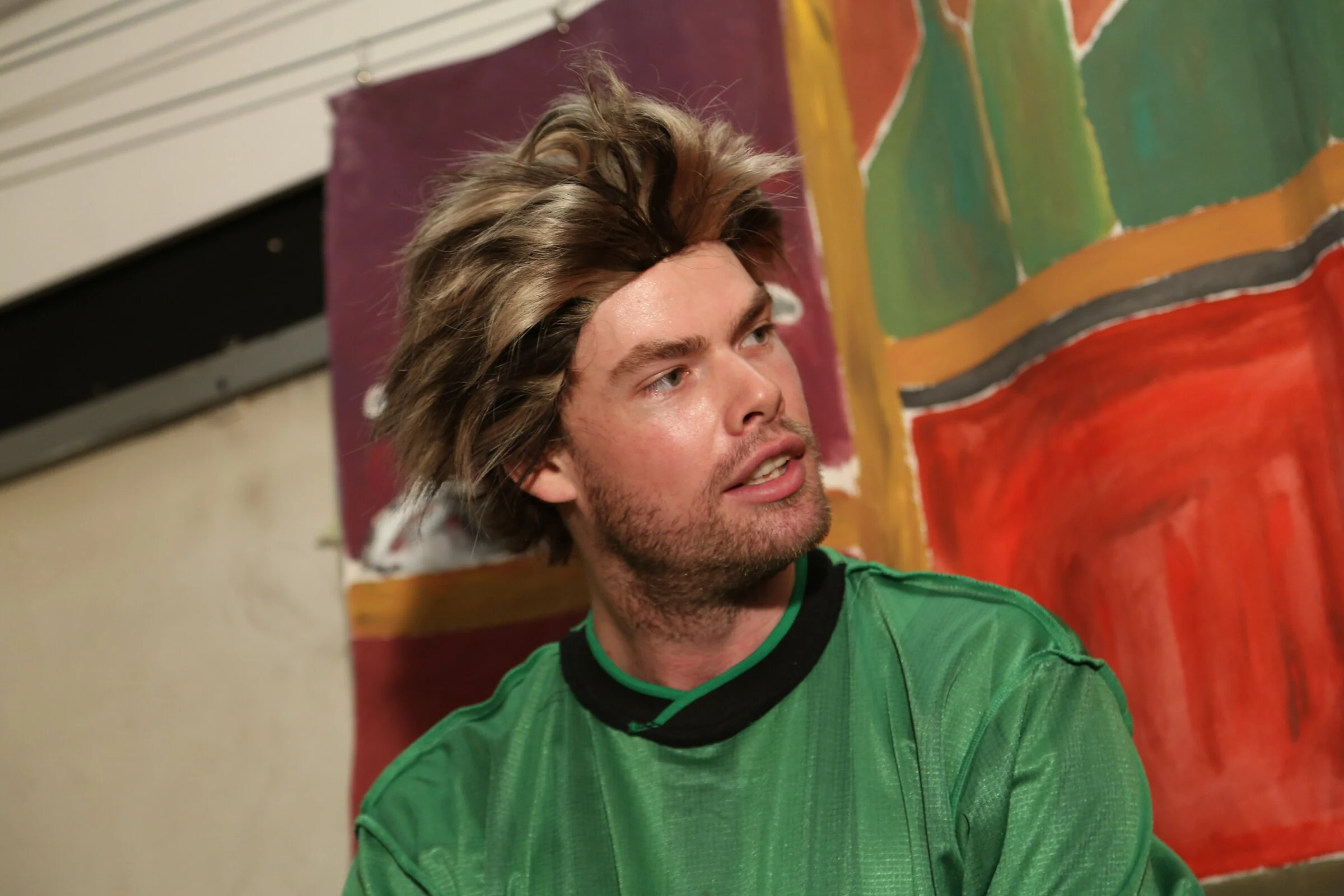 A close-up of a performer in a short wig and green shirt.