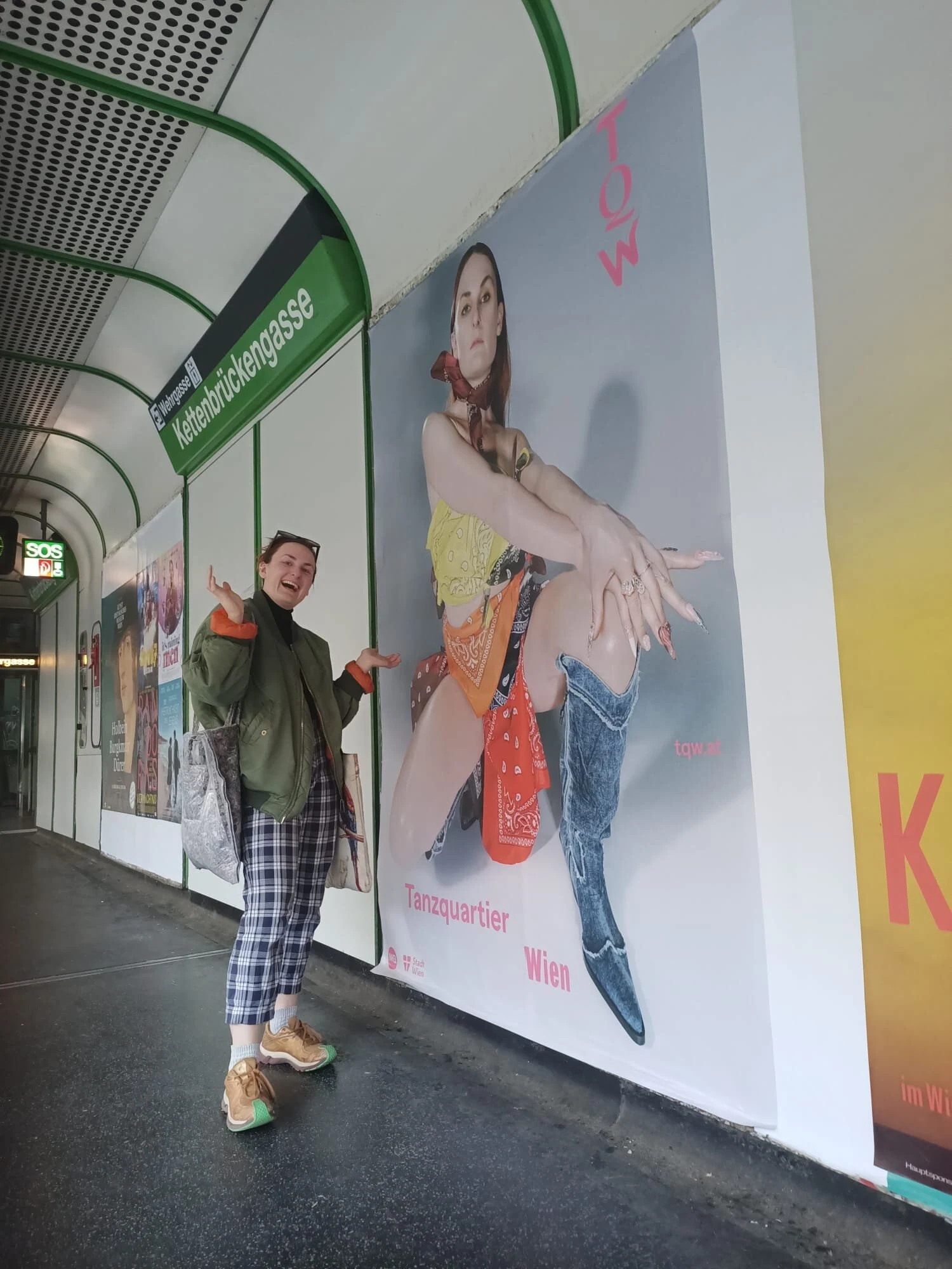 A person posing beside the large bandana portrait poster at Kettenbrueckengasse station.