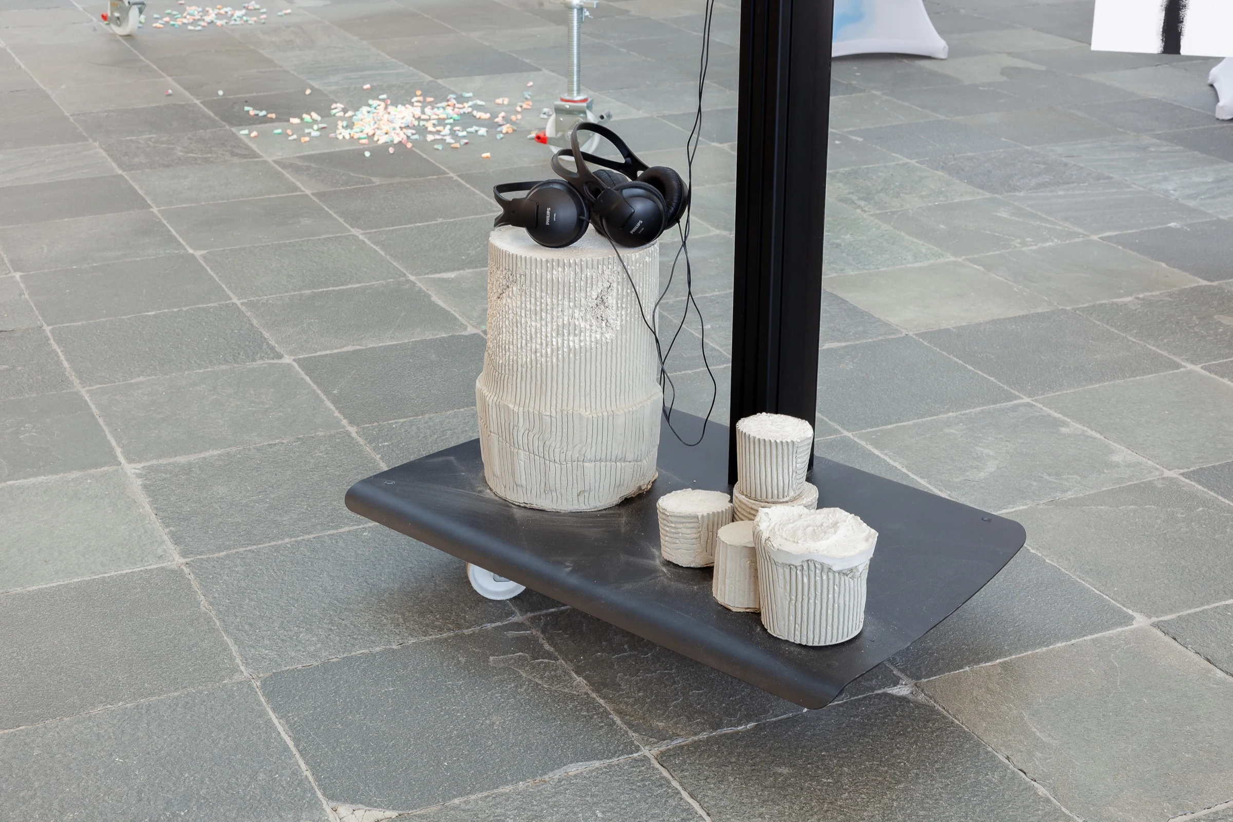 Headphones resting on white textured cylinders on a black wheeled platform.