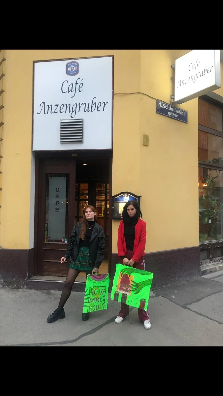 Two performers holding fluorescent green bags outside Café Anzengruber.