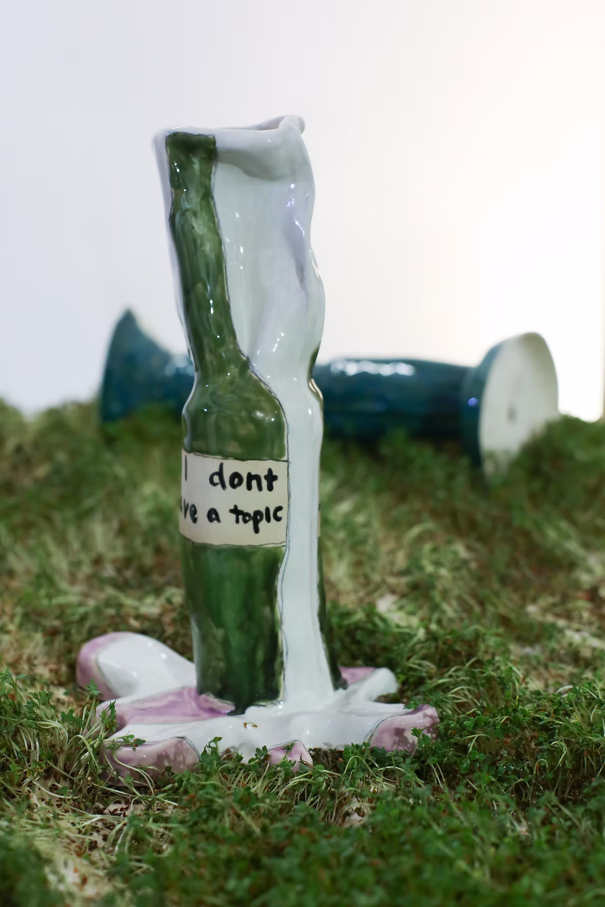 Handmade green and white bottles displayed on grass, with a handwritten label on the foreground bottle.