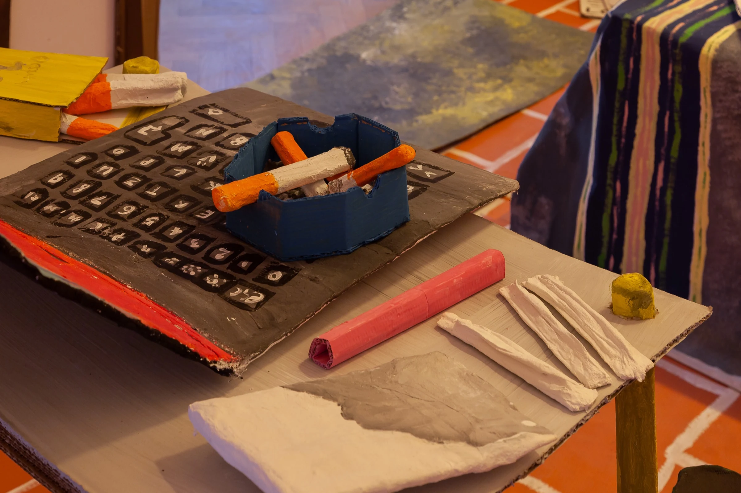 A close-up of a handmade cardboard laptop, ashtray and paper on a table.