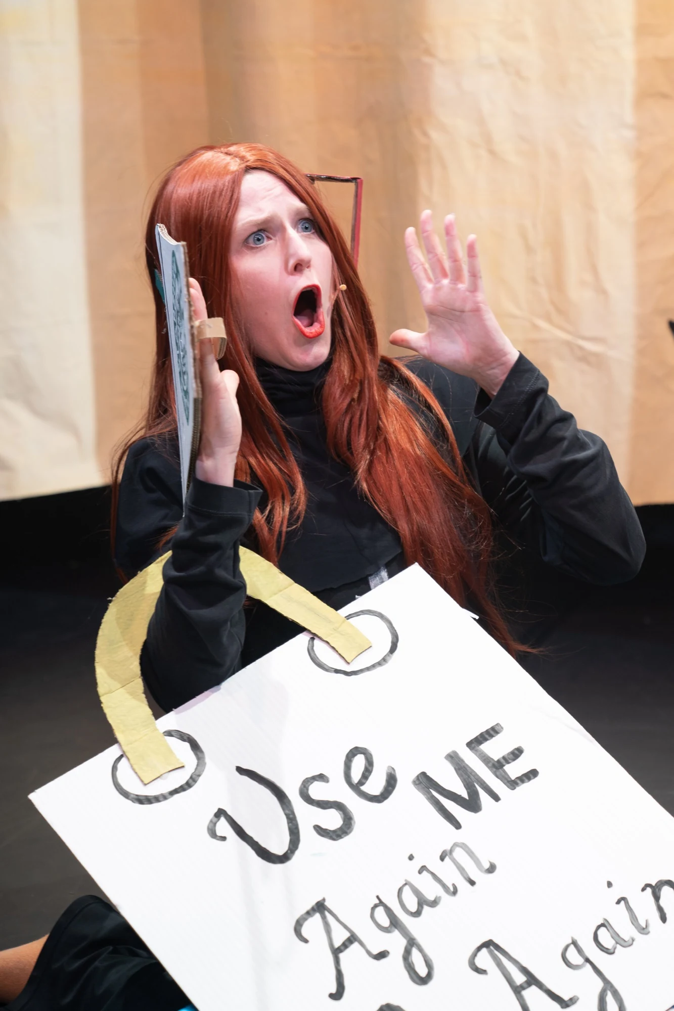 Charlotte reacting with raised hands beside a handmade cardboard bag.