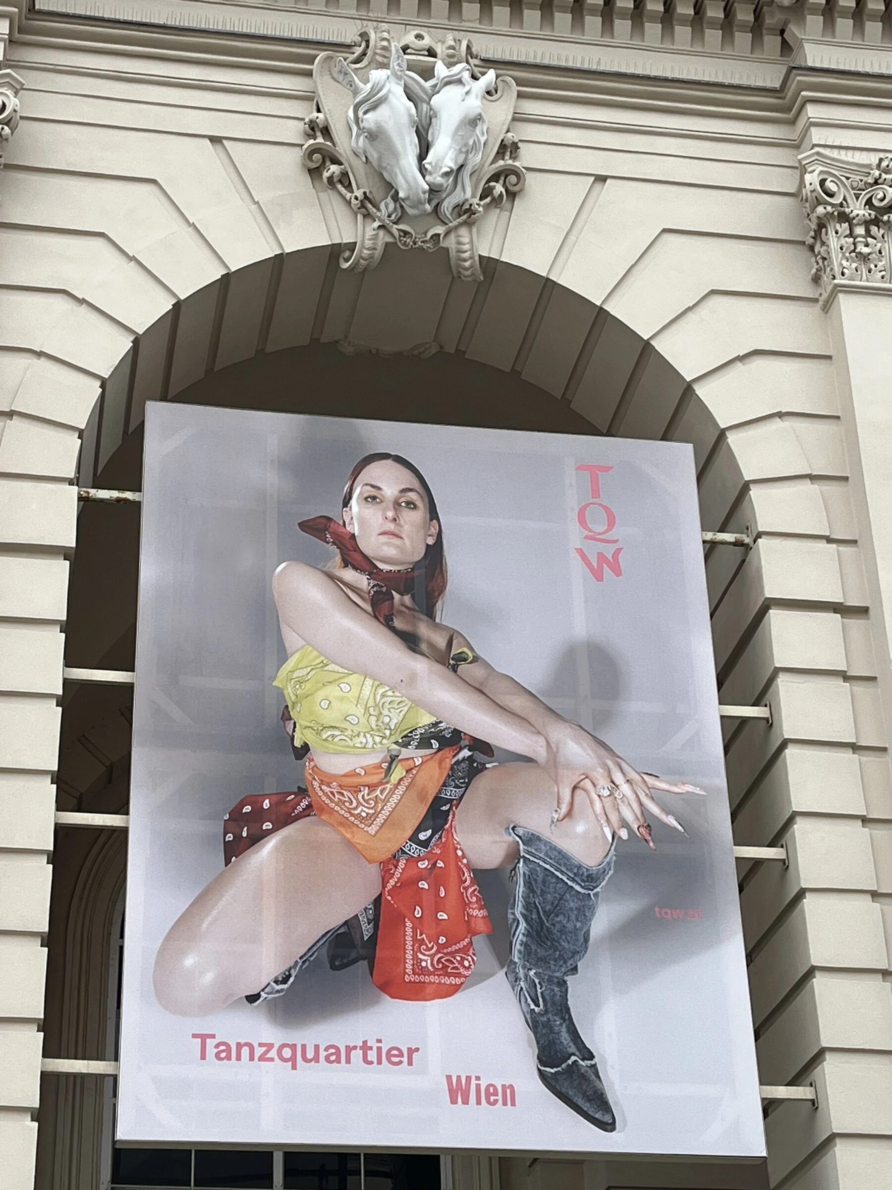 A close-up of the Tanzquartier portrait poster beneath a sculpted face on the building facade.