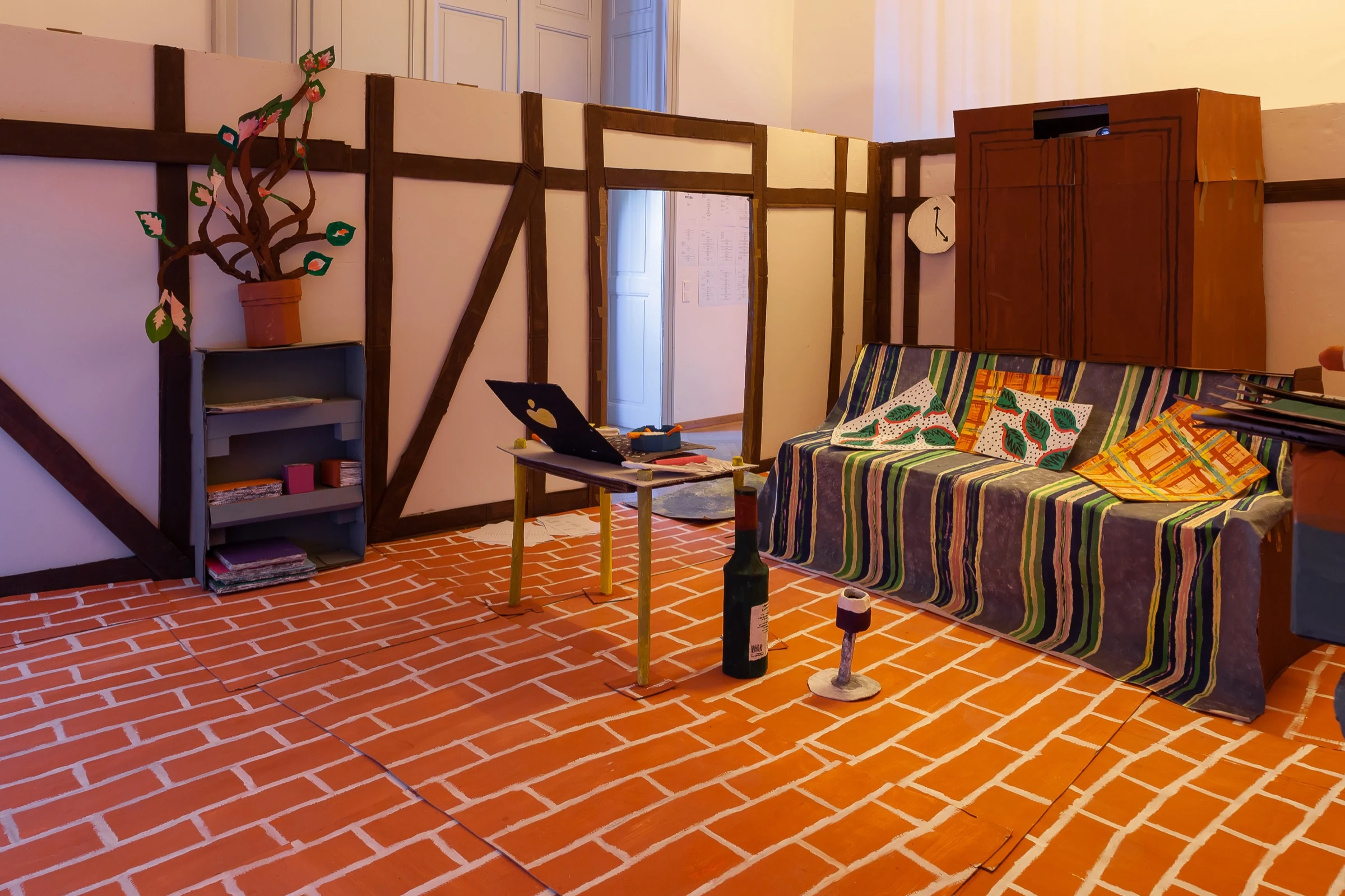A wide view of the cardboard apartment with striped sofa, low table and kitchen counter.