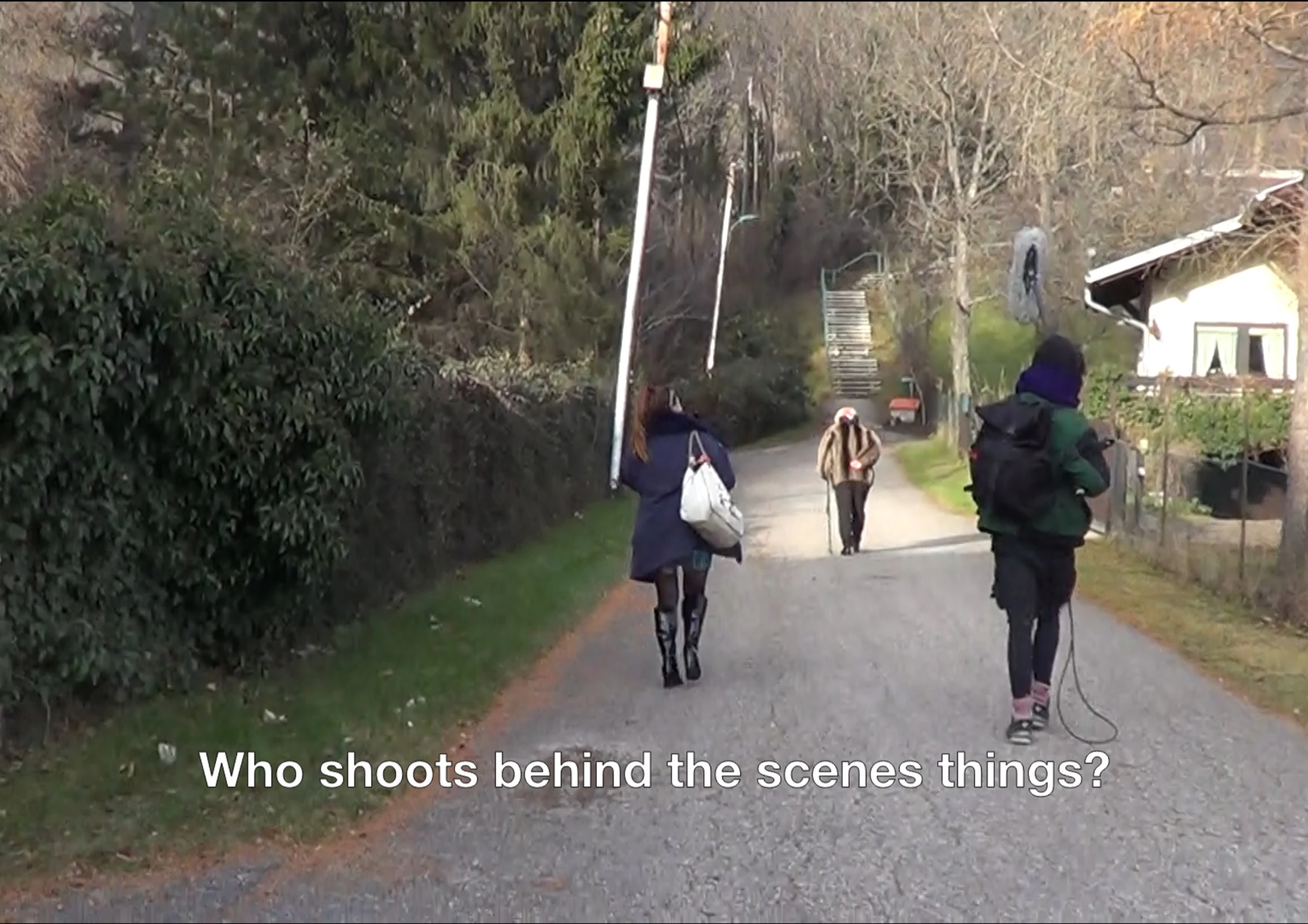 A film crew recording a performer on a quiet road beside trees and houses.