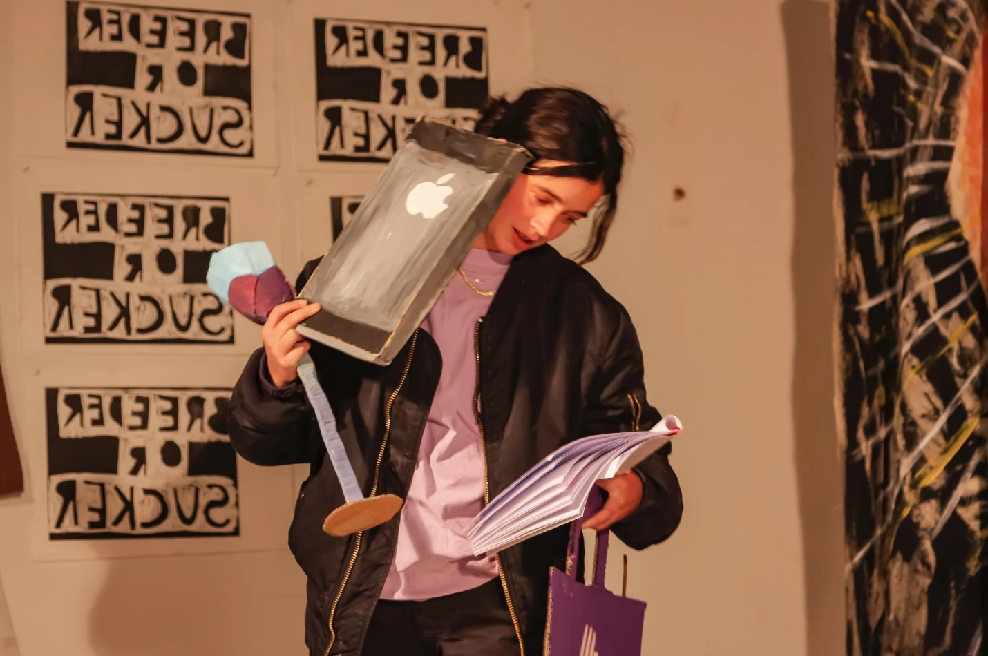 A performer reading a script while holding an oversized cardboard phone and shopping bag.