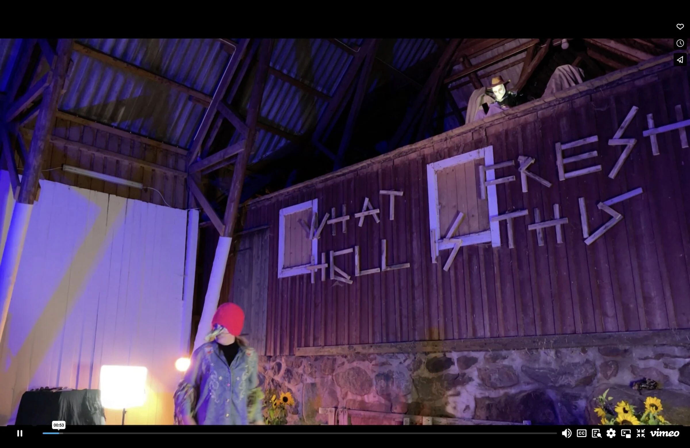 A performer in a red hat beneath a masked performer reading from the barn loft.