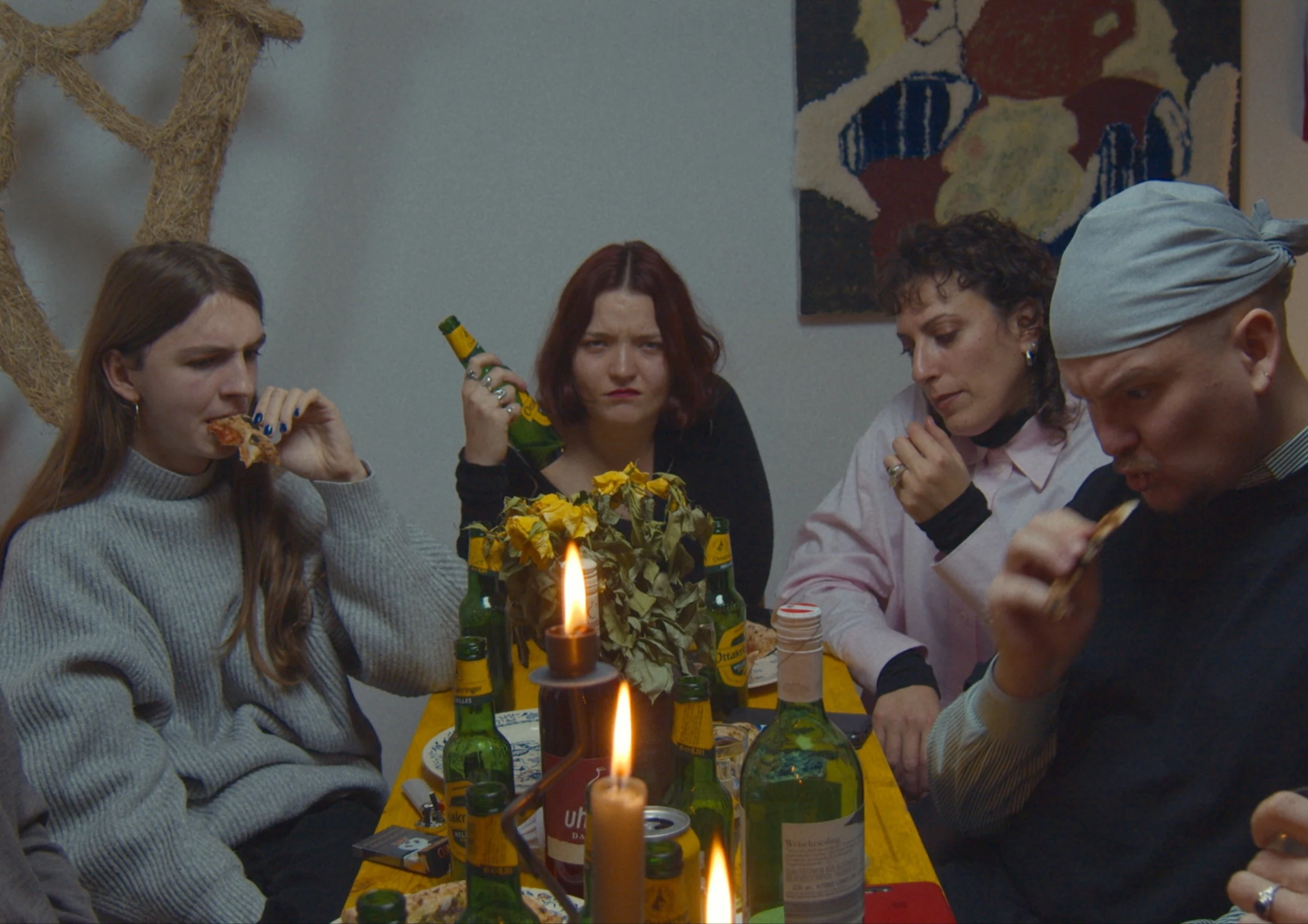 Four friends eating pizza around a table lit by candles.