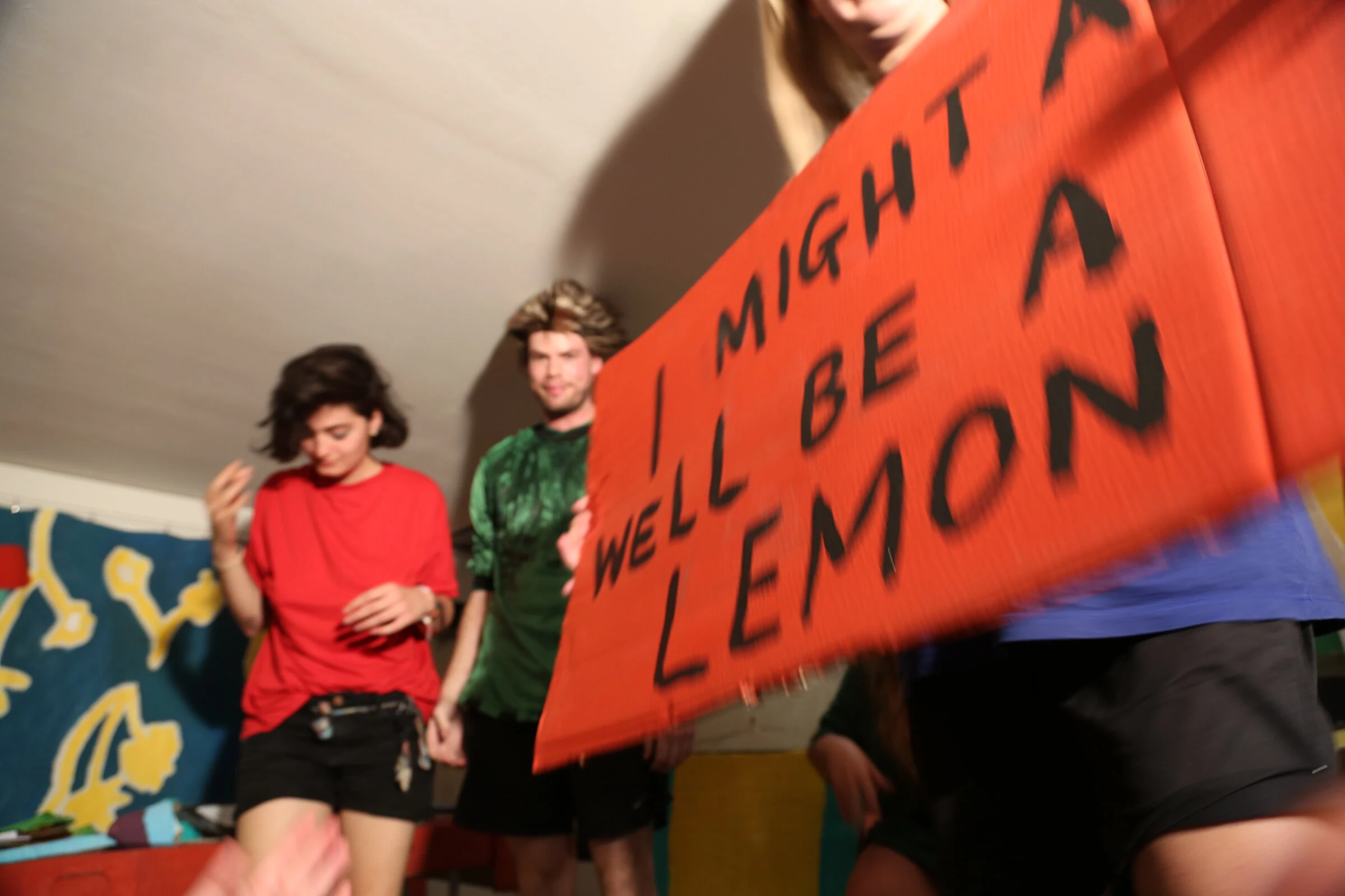 Performers holding a red cardboard sign reading I Might as Well Be a Lemon.