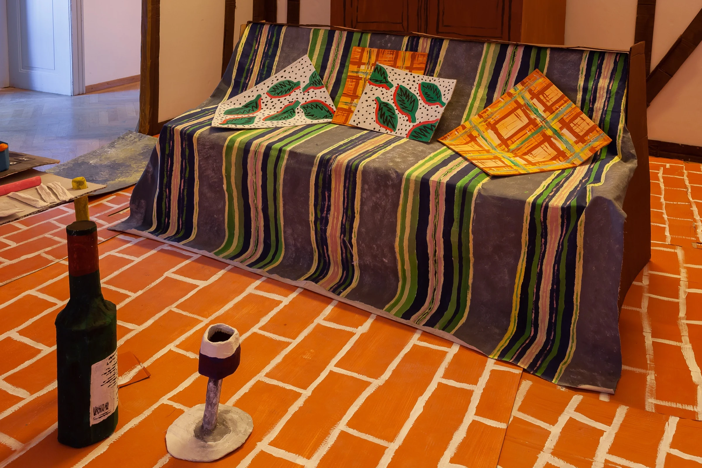 The striped cardboard sofa with painted cushions and handmade bottles in the foreground.