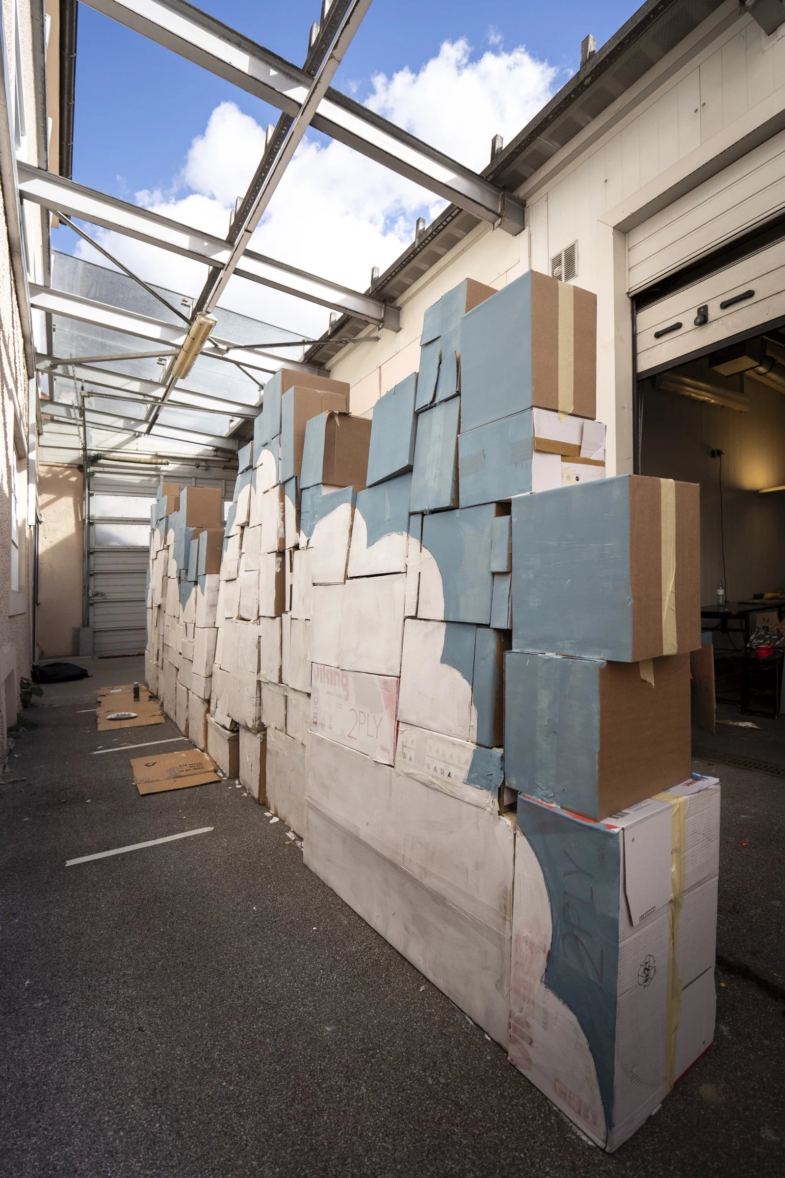 A wall of cardboard boxes painted with a blue sky and white clouds.